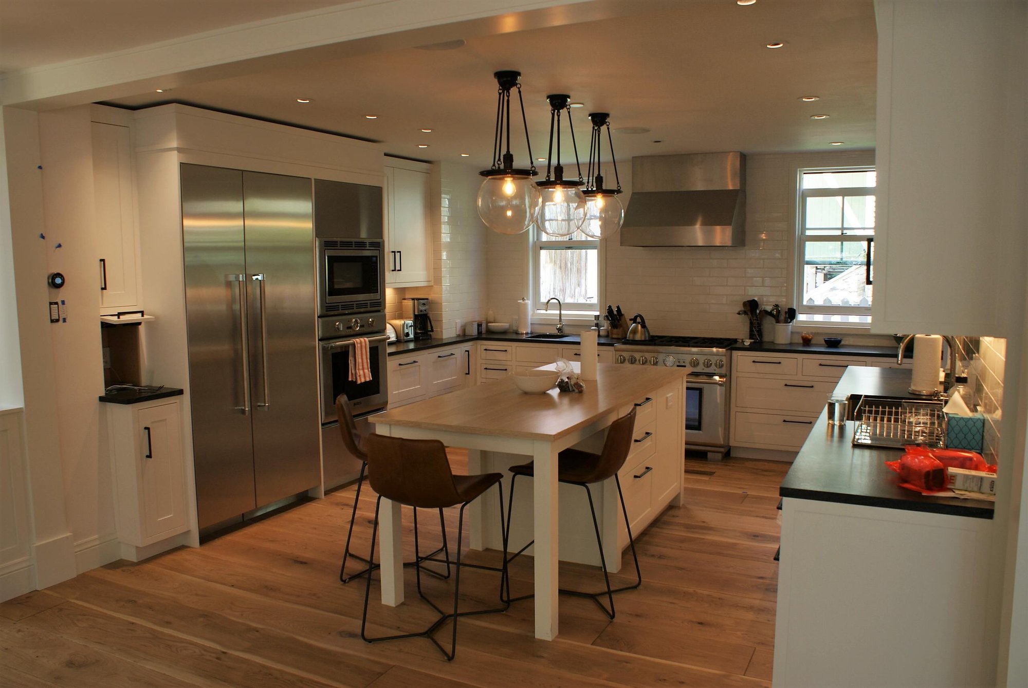 Mid-sized farmhouse u-shaped medium tone wood floor eat-in kitchen with shaker cabinets, white cabinets, soapstone countertops, white backsplash, subway tile backsplash, stainless steel appliances and an island, by Jensen Design in Telluride, CO