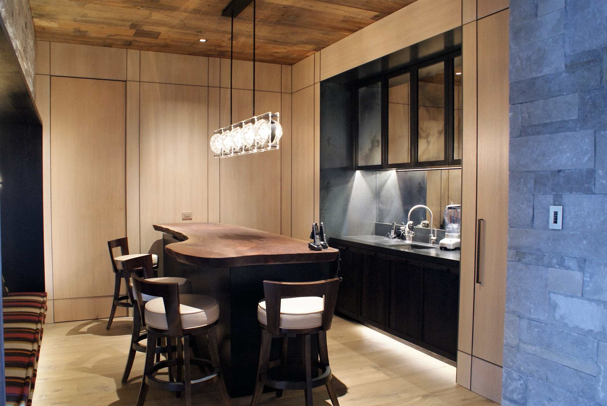 Mid-sized transitional galley light wood floor seated home bar with an undermount sink, shaker cabinets, black cabinets, solid surface countertops and mirror backsplash, by Jensen Design in Telluride, CO