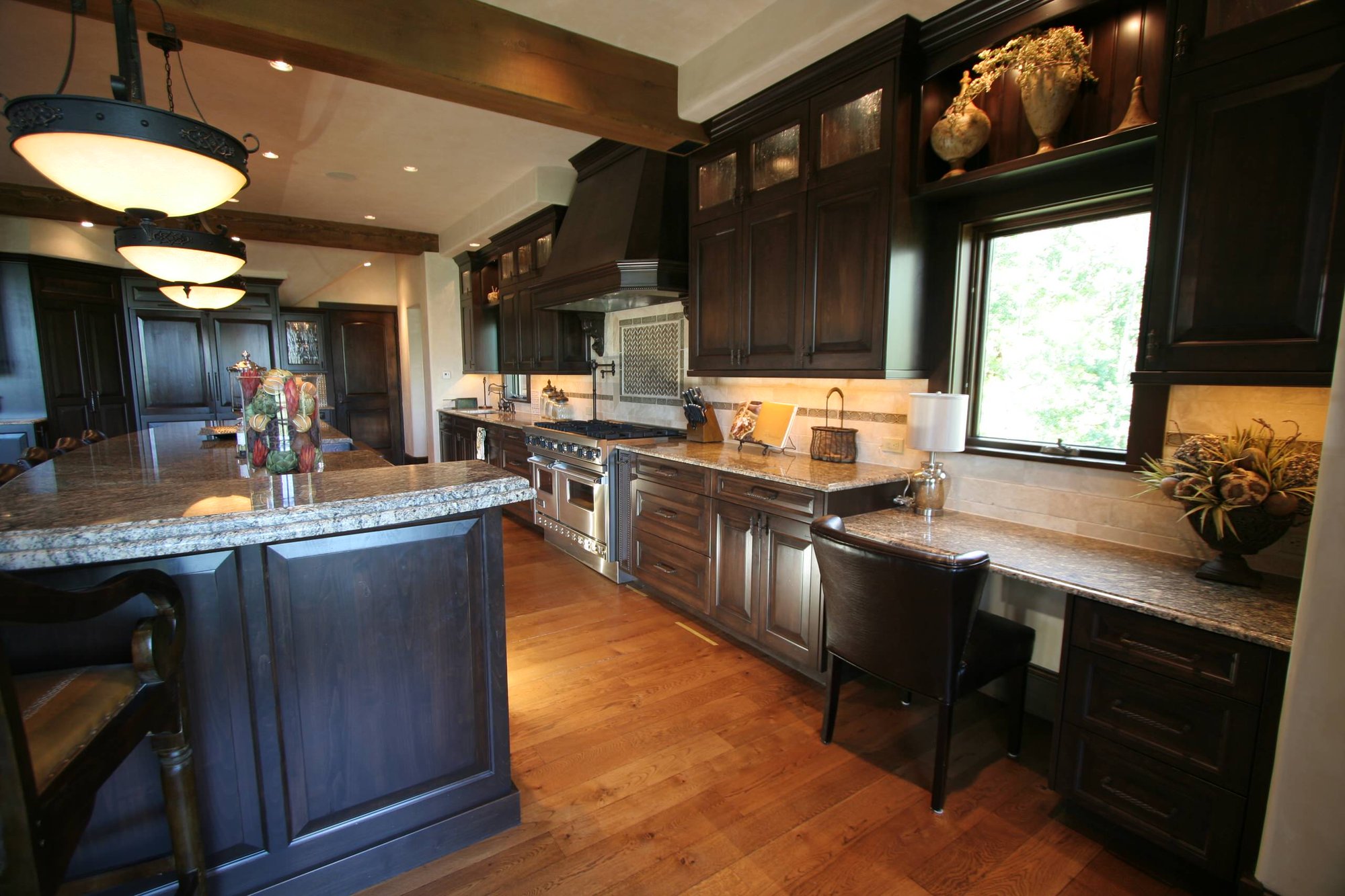 Large traditional l-shaped medium tone wood floor eat-in kitchen with raised-panel cabinets, paneled appliances, an island, a farmhouse sink, dark wood cabinets, granite countertops, beige backsplash and ceramic backsplash, by Jensen Design in Telluride, CO