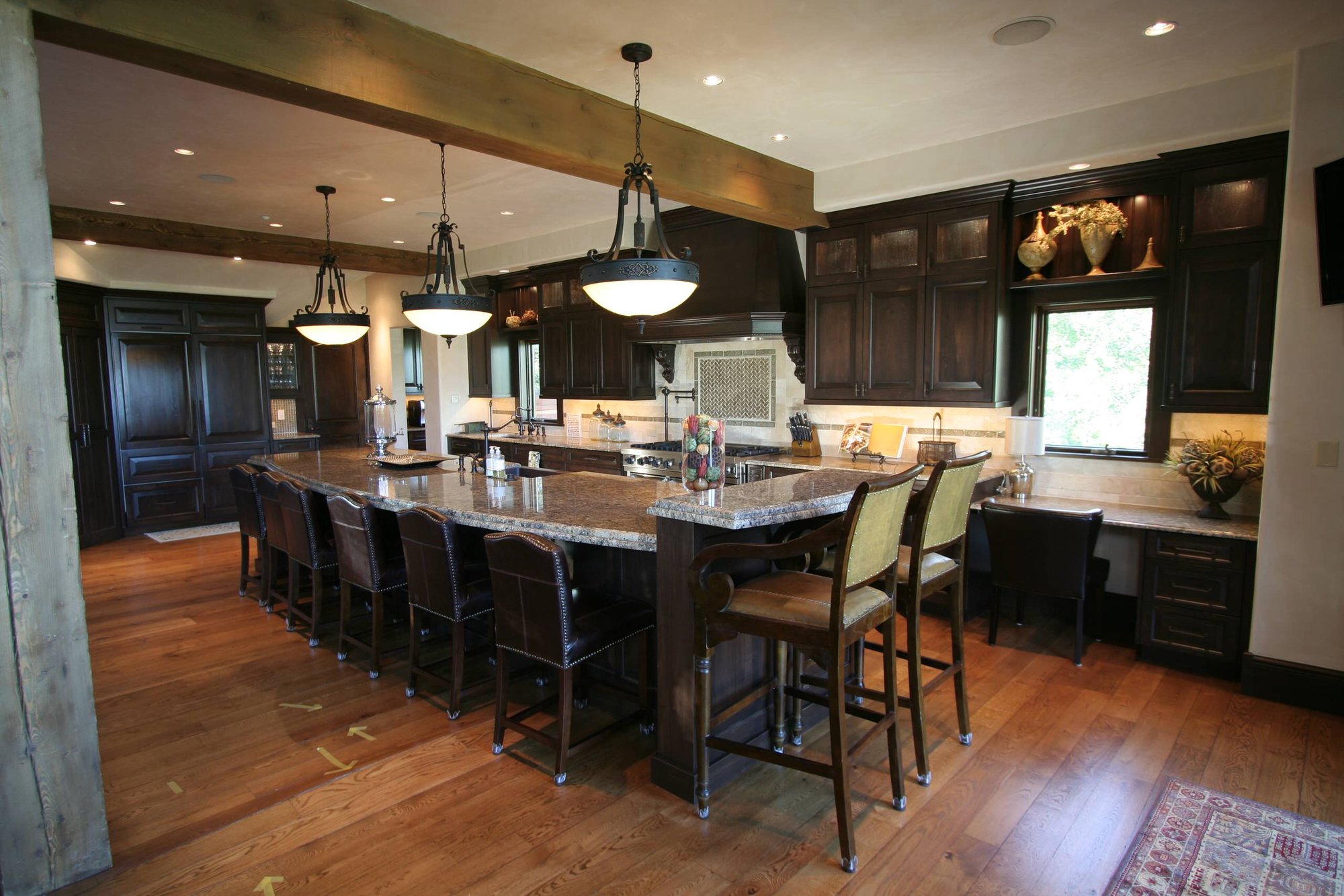 Large elegant l-shaped medium tone wood floor eat-in kitchen with raised-panel cabinets, dark wood cabinets, paneled appliances, a farmhouse sink, granite countertops, beige backsplash, ceramic backsplash and an island, by Jensen Design in Telluride, CO