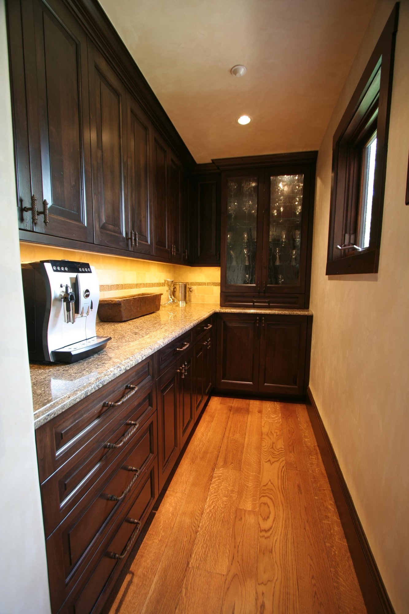 Large elegant l-shaped medium tone wood floor eat-in kitchen with raised-panel cabinets, dark wood cabinets, a farmhouse sink, granite countertops, beige backsplash, ceramic backsplash, paneled appliances and an island, by Jensen Design in Telluride, CO
