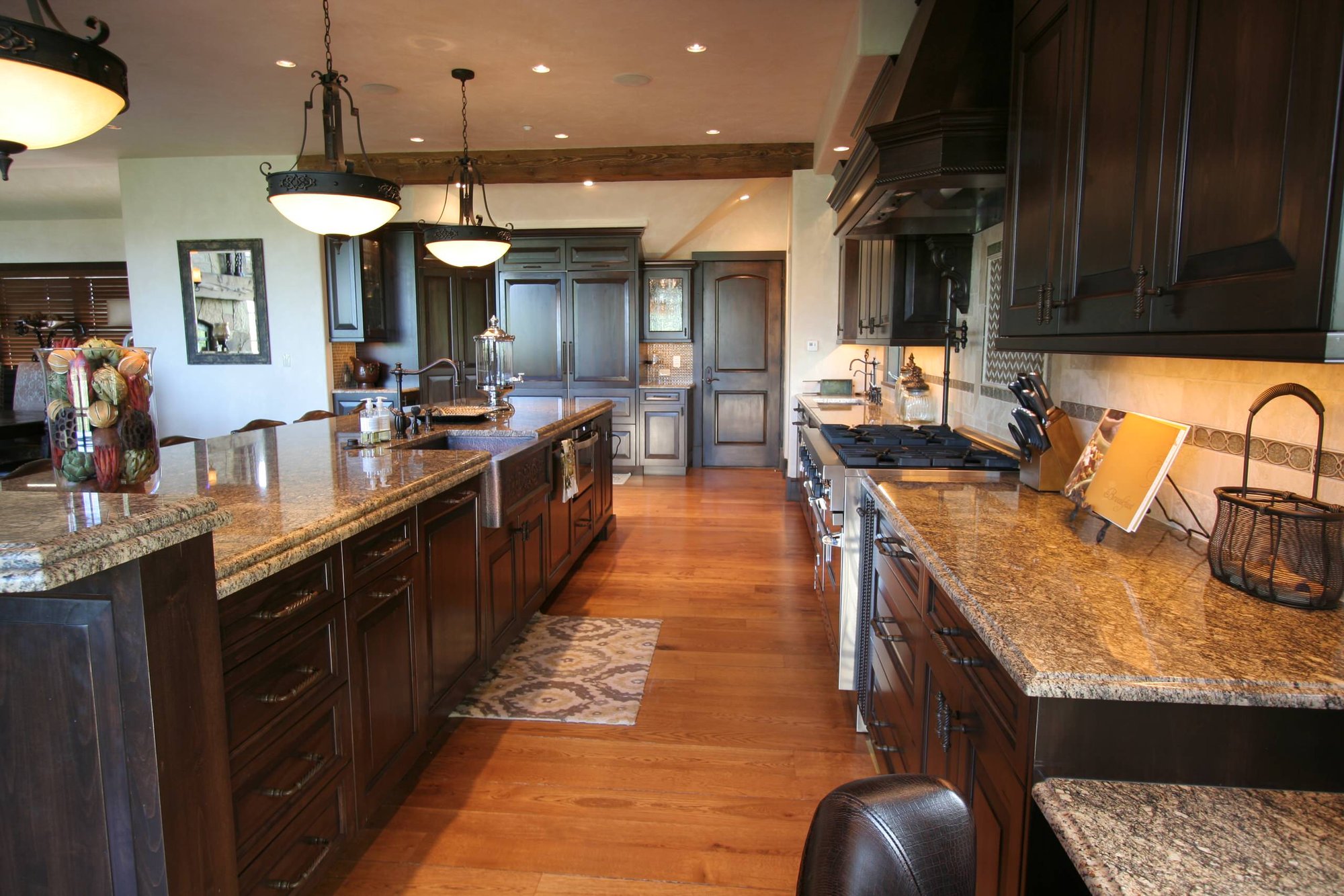 Large elegant l-shaped medium tone wood floor eat-in kitchen with a farmhouse sink, raised-panel cabinets, dark wood cabinets, paneled appliances, an island, granite countertops, beige backsplash and ceramic backsplash, by Jensen Design in Telluride, CO