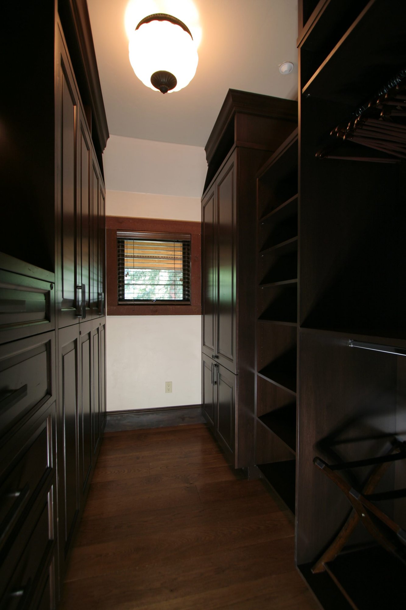 Mid-sized classic gender-neutral dark wood floor walk-in closet with raised-panel cabinets and dark wood cabinets, by Jensen Design in Telluride, CO