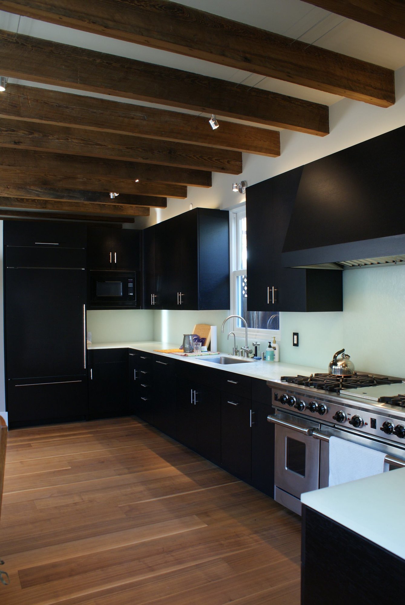 Mid-sized modern l-shaped dark wood floor eat-in kitchen with an undermount sink, flat-panel cabinets, black cabinets, glass countertops, white backsplash, glass sheet backsplash, stainless steel appliances and no island, by Jensen Design in Telluride, CO