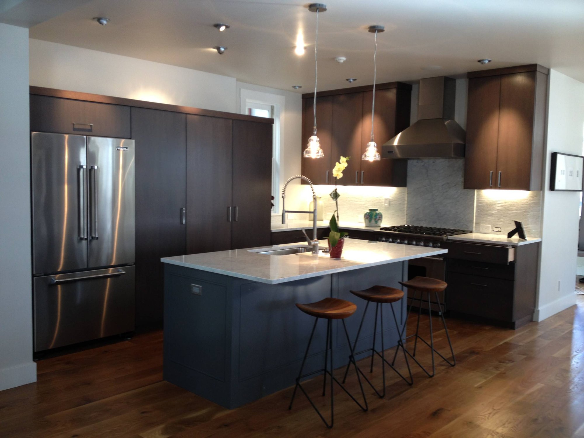 Mid-sized trendy l-shaped dark wood floor open concept kitchen with an undermount sink, flat-panel cabinets, dark wood cabinets, quartzite countertops, white backsplash, stainless steel appliances, an island and stone slab backsplash, by Jensen Design in Telluride, CO