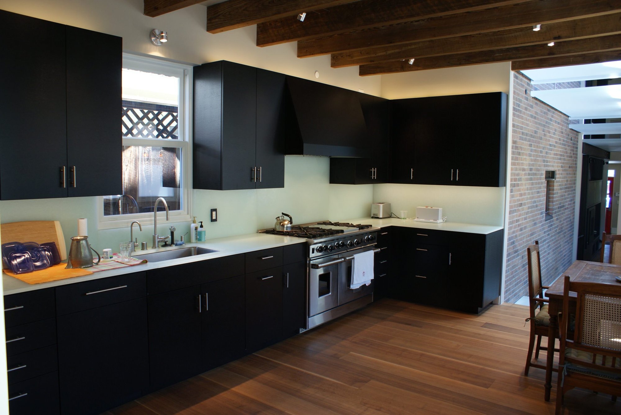 Mid-sized modern l-shaped dark wood floor eat-in kitchen with an undermount sink, flat-panel cabinets, black cabinets, glass countertops, white backsplash, glass sheet backsplash, stainless steel appliances and no island, by Jensen Design in Telluride, CO