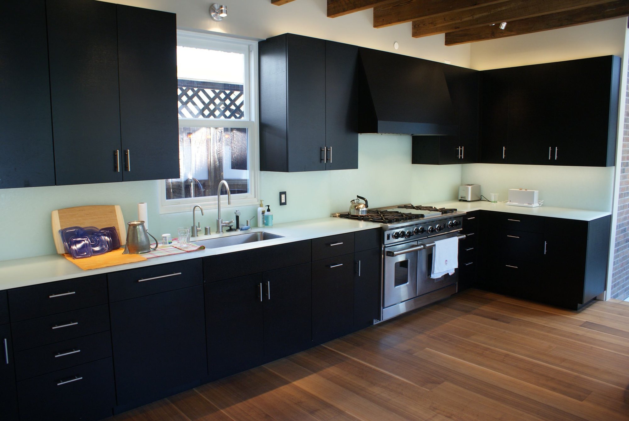 Mid-sized minimalist l-shaped dark wood floor eat-in kitchen with an undermount sink, flat-panel cabinets, black cabinets, glass countertops, white backsplash, glass sheet backsplash, stainless steel appliances and no island, by Jensen Design in Telluride, CO