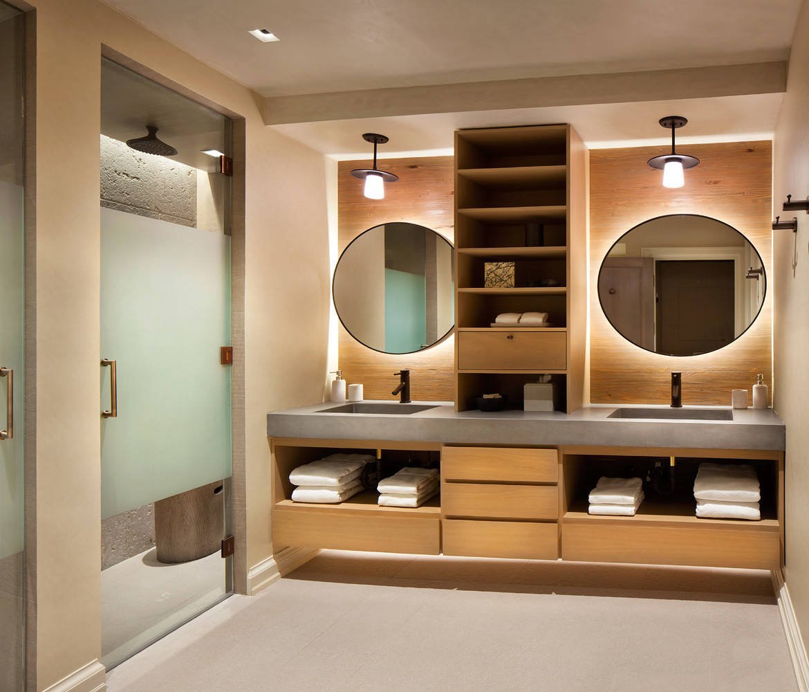 Rustic alcove shower with flat-panel cabinets, medium tone wood cabinets, beige walls, an integrated sink, concrete countertops and a hinged shower door, by Jensen Design in Telluride, CO