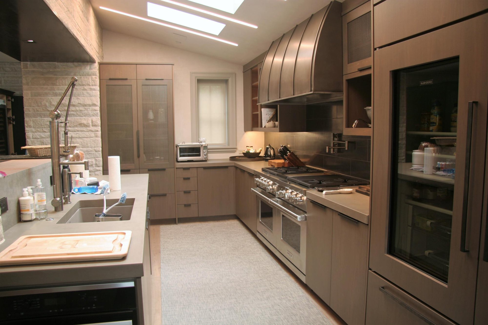 Mid-sized modern l-shaped light wood floor open concept kitchen with an undermount sink, flat-panel cabinets, an island, brown cabinets, gray backsplash, porcelain backsplash and stainless steel appliances, by Jensen Design in Telluride, CO