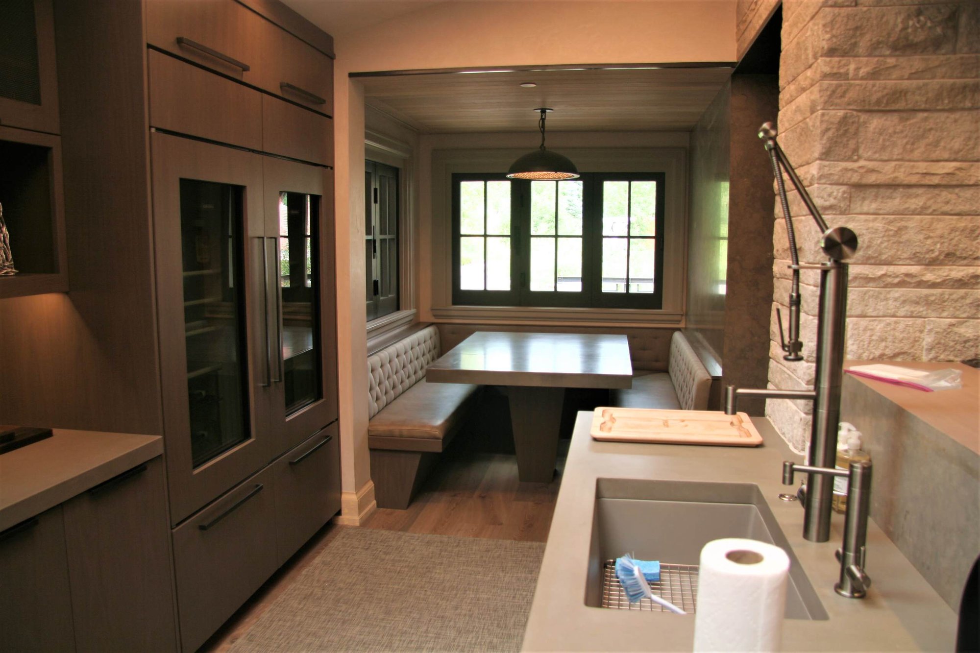 Mid-sized modern l-shaped light wood floor open concept kitchen with an undermount sink, flat-panel cabinets, an island, brown cabinets, gray backsplash, porcelain backsplash and stainless steel appliances, by Jensen Design in Telluride, CO
