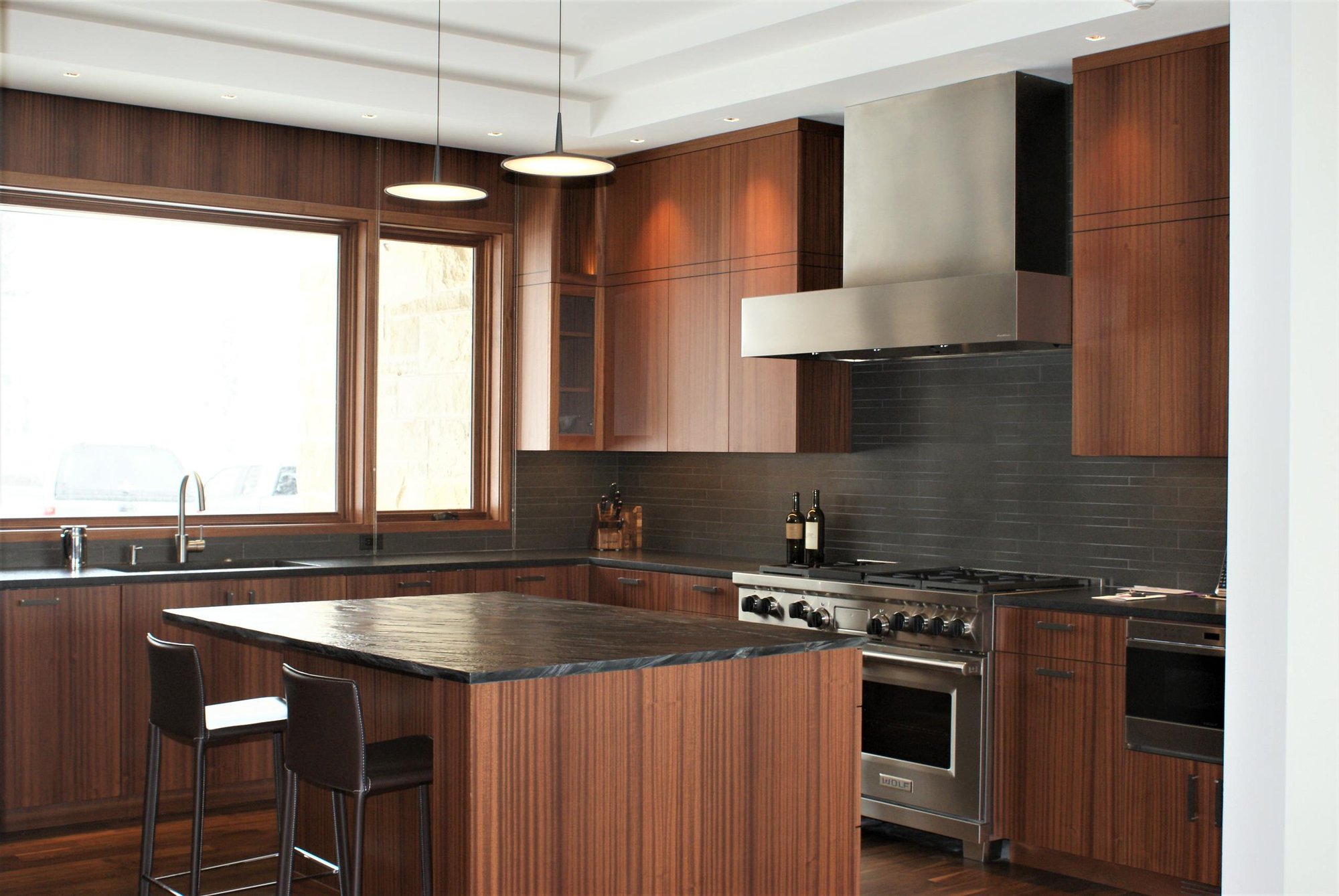 Large trendy u-shaped dark wood floor eat-in kitchen with an undermount sink, flat-panel cabinets, medium tone wood cabinets, black backsplash, stainless steel appliances, an island, soapstone countertops and porcelain backsplash, by Jensen Design in Telluride, CO