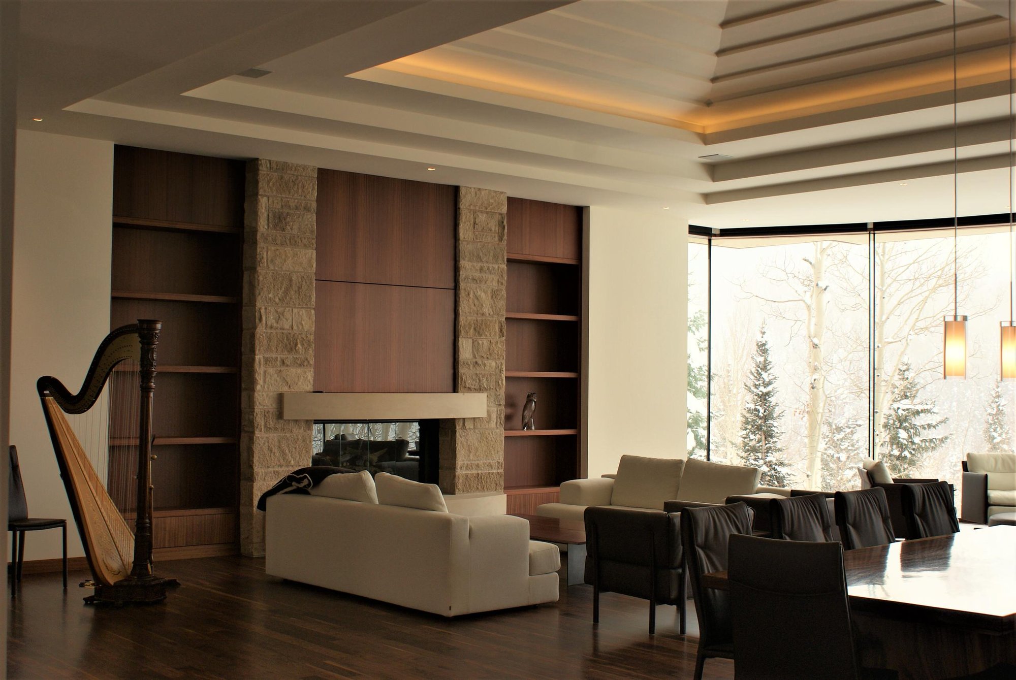 Large contemporary formal and open concept dark wood floor living room with a standard fireplace, a stone fireplace, a concealed tv and beige walls, by Jensen Design in Telluride, CO