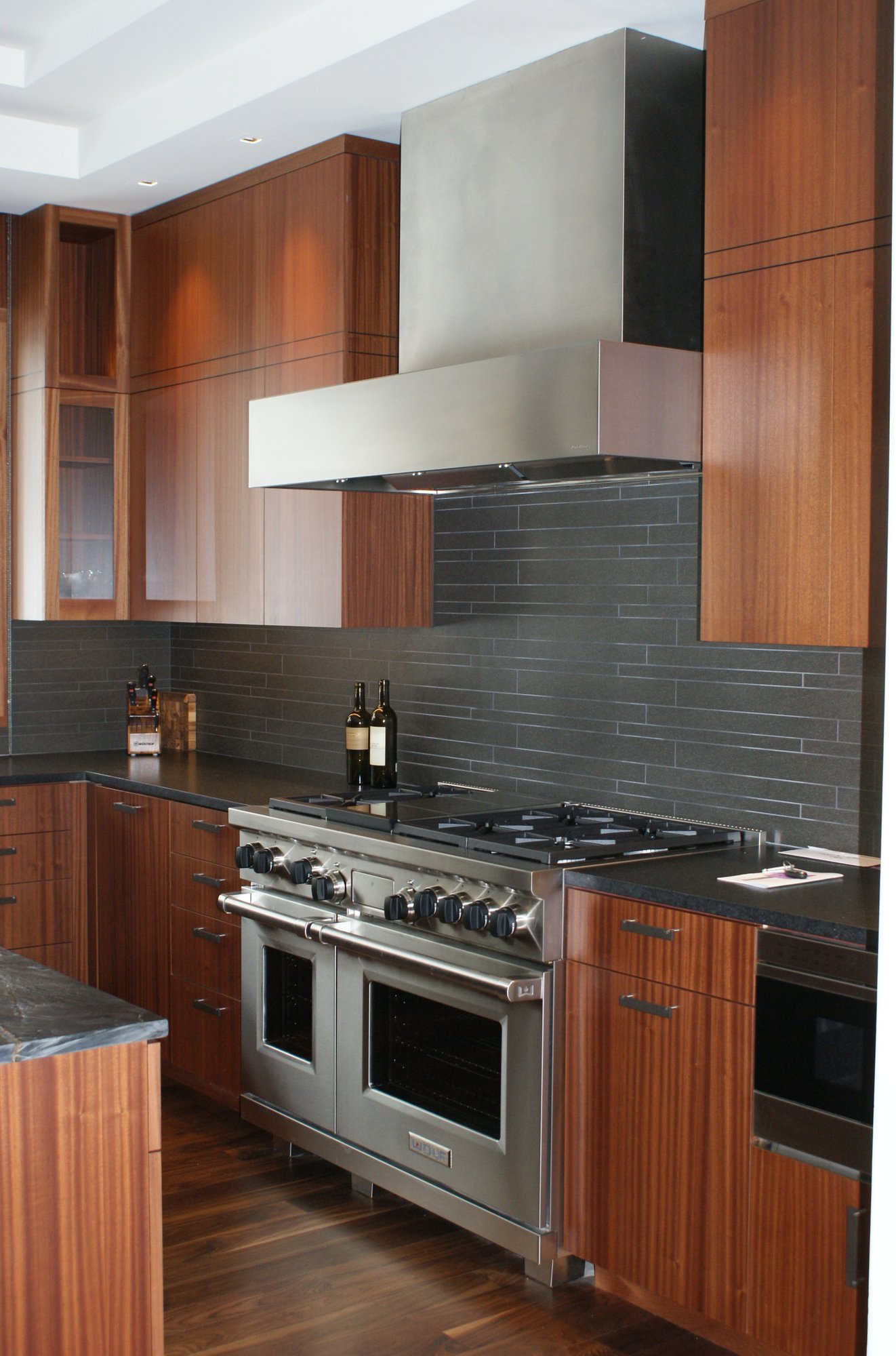 Large contemporary u-shaped dark wood floor eat-in kitchen with an undermount sink, flat-panel cabinets, medium tone wood cabinets, black backsplash, stainless steel appliances, an island, soapstone countertops and porcelain backsplash, by Jensen Design in Telluride, CO