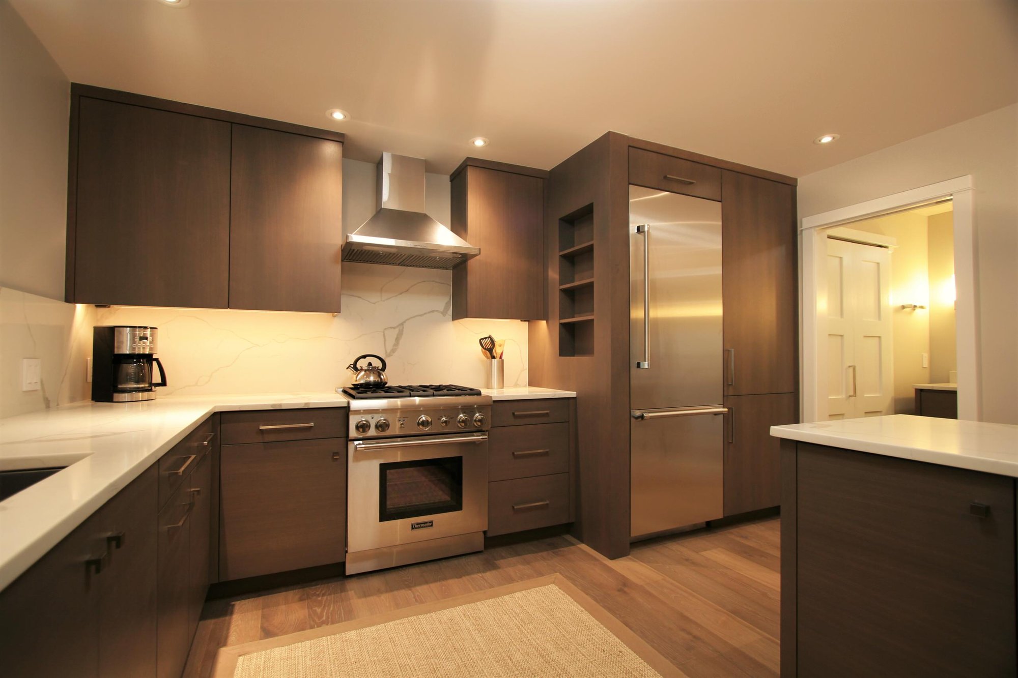 Mid-sized trendy u-shaped medium tone wood floor open concept kitchen with flat-panel cabinets, medium tone wood cabinets, marble countertops, white backsplash, marble backsplash, stainless steel appliances and a peninsula, by Jensen Design in Telluride, CO
