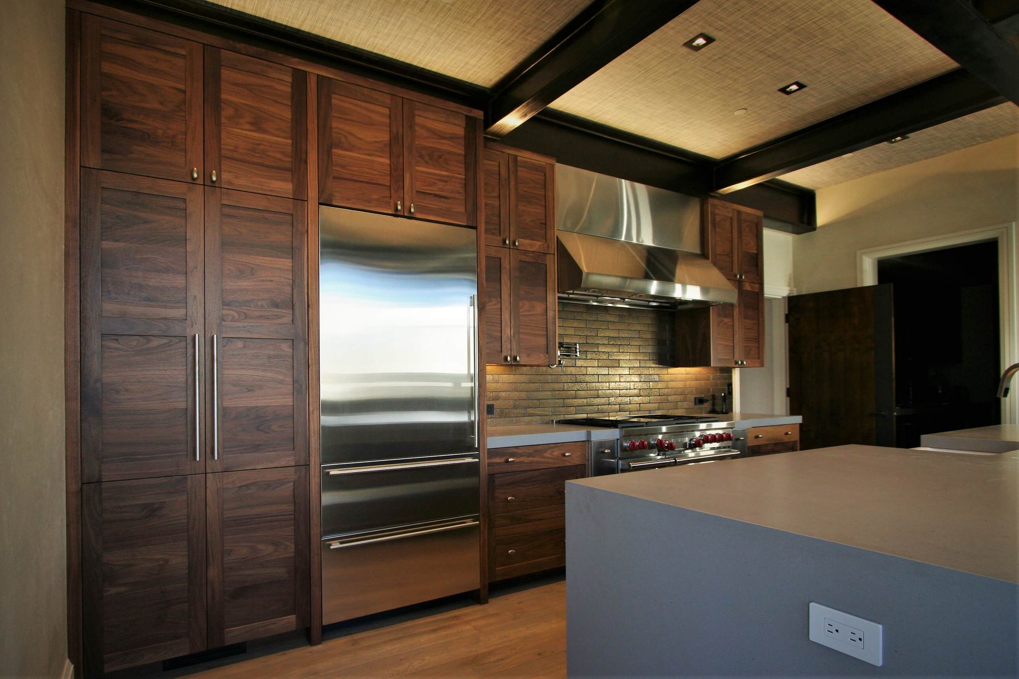 Mid-sized trendy galley light wood floor and brown floor open concept kitchen with a farmhouse sink, shaker cabinets, medium tone wood cabinets, concrete countertops, stainless steel appliances, an island, brown backsplash and stone tile backsplash, by Jensen Design in Mountain Village, CO