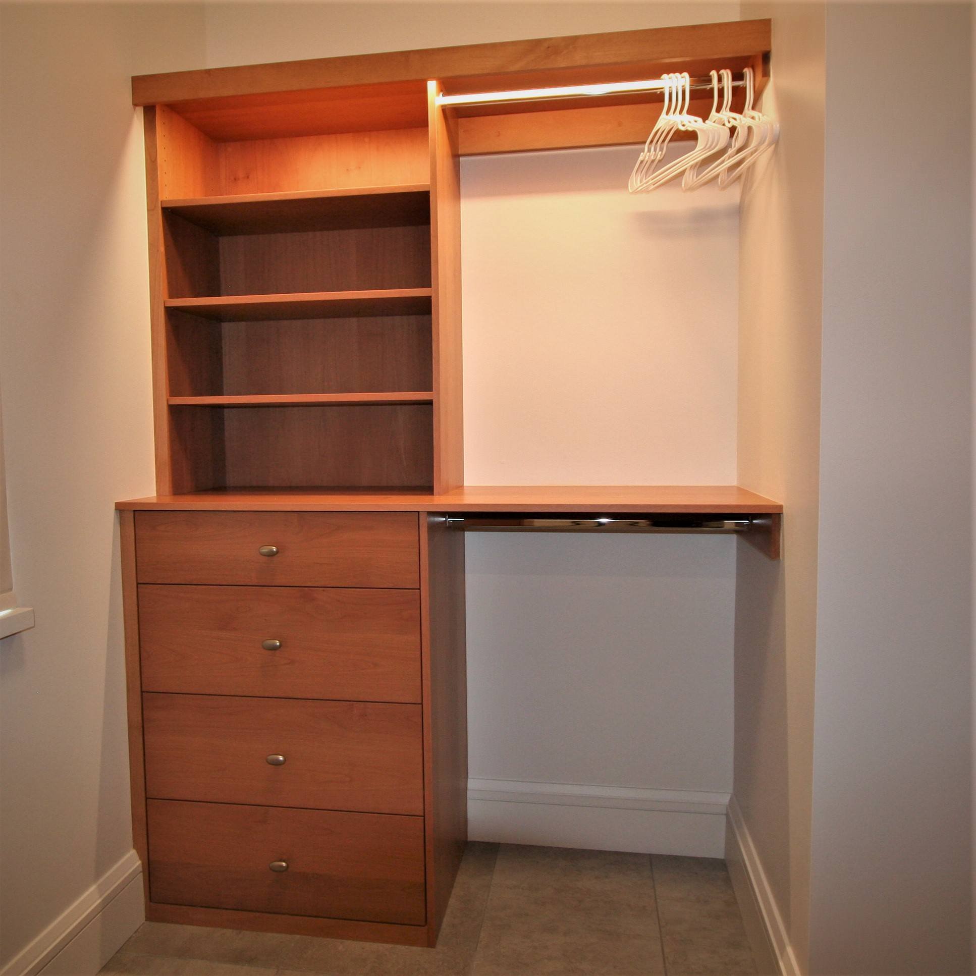 Small timeless gender-neutral ceramic tile and beige floor walk-in closet with flat-panel cabinets and medium tone wood cabinets, by Jensen Design in Mountain Village, CO