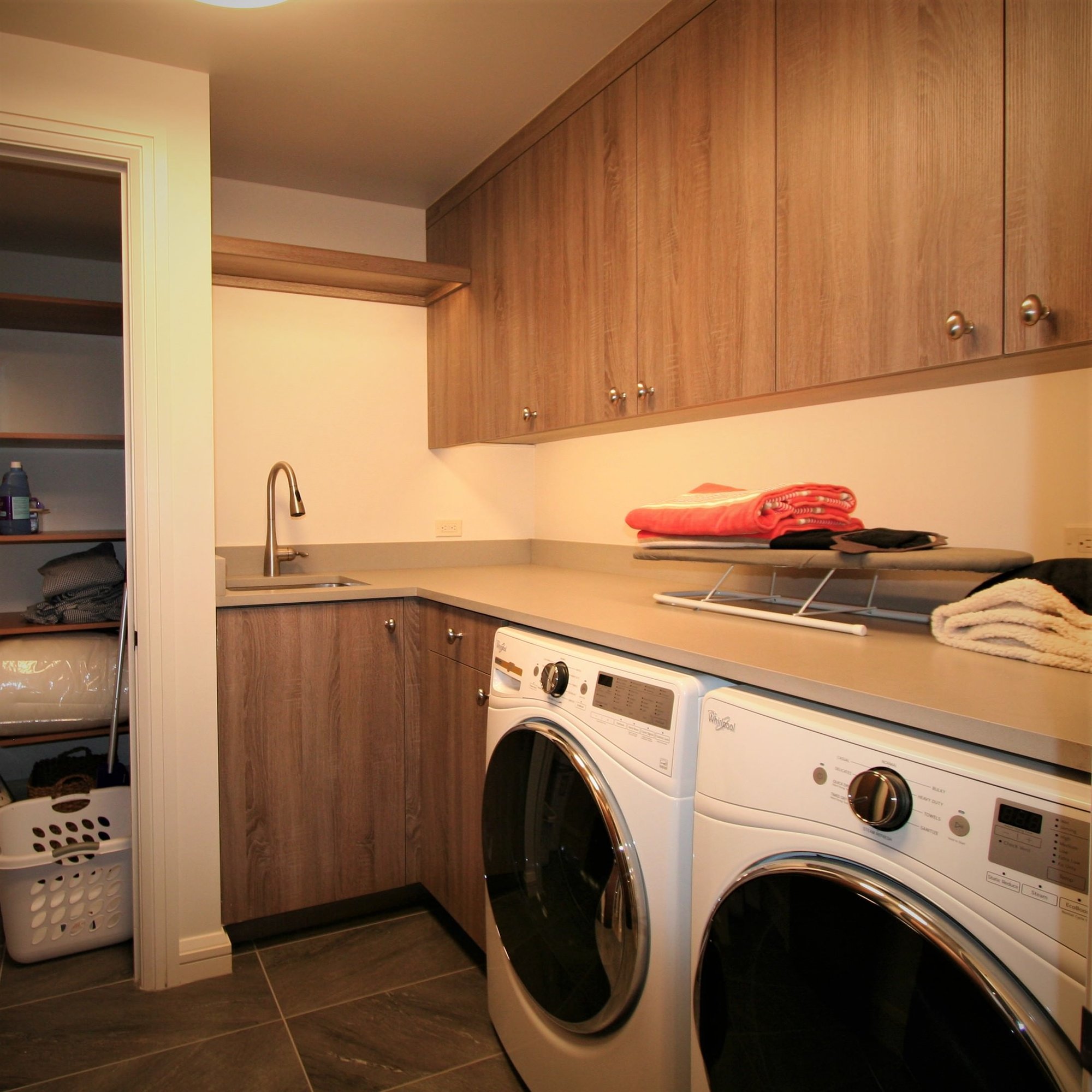 Mid-sized contemporary l-shaped ceramic tile dedicated laundry room with an undermount sink, flat-panel cabinets, medium tone wood cabinets, a side-by-side washer/dryer and beige walls, by Jensen Design in Mountain Village, CO