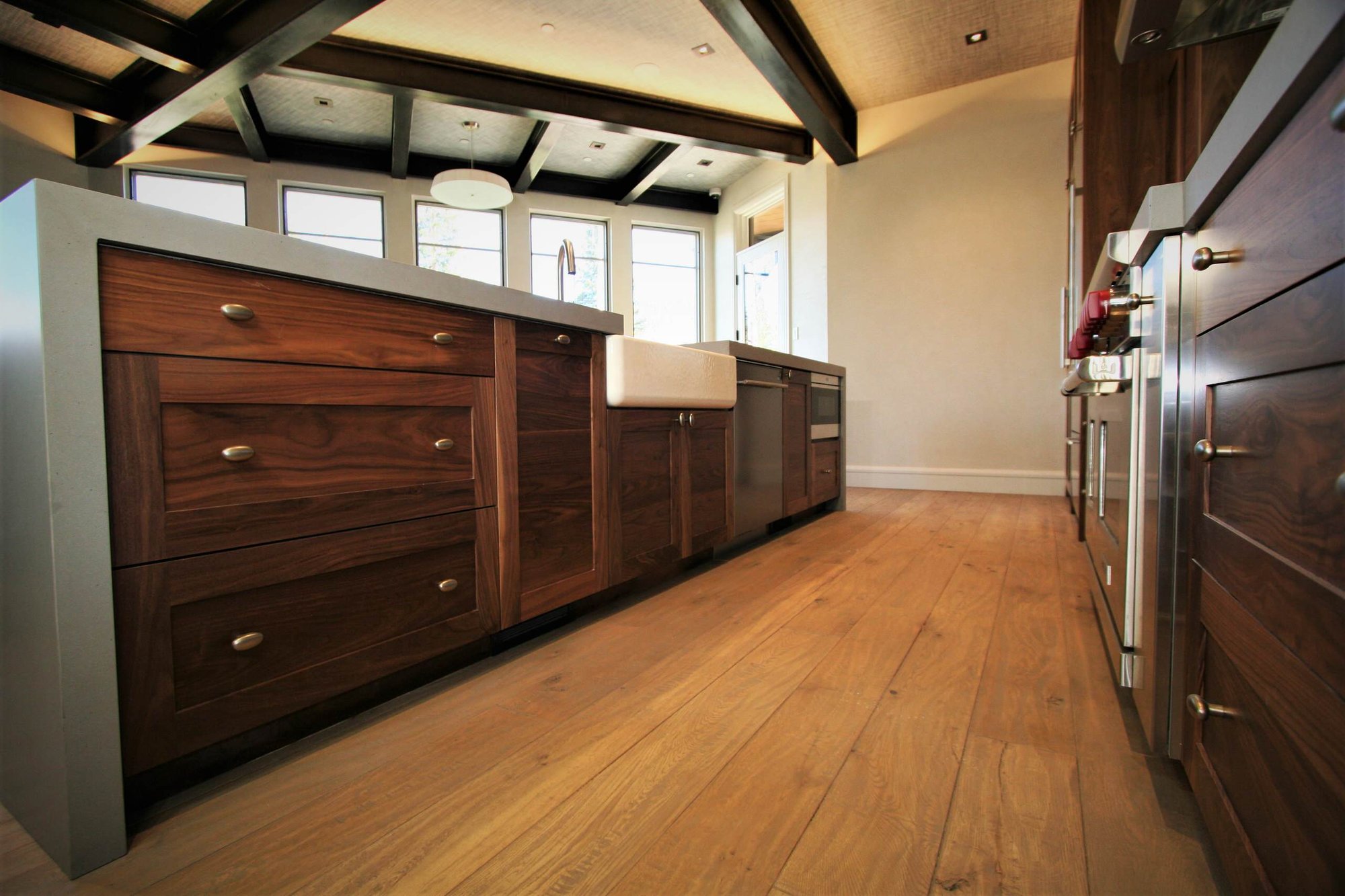 Mid-sized trendy galley light wood floor and brown floor open concept kitchen with a farmhouse sink, shaker cabinets, medium tone wood cabinets, concrete countertops, stainless steel appliances, an island, brown backsplash and stone tile backsplash, by Jensen Design in Mountain Village, CO
