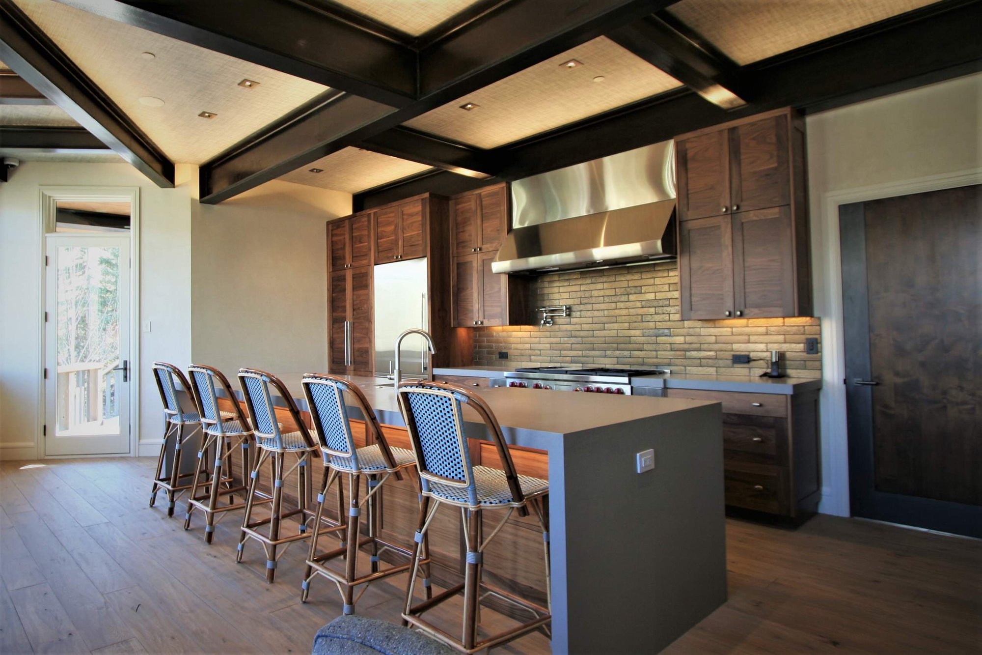 Mid-sized contemporary galley light wood floor and brown floor open concept kitchen with a farmhouse sink, shaker cabinets, medium tone wood cabinets, concrete countertops, stainless steel appliances, an island, brown backsplash and stone tile backsplash, by Jensen Design in Mountain Village, CO