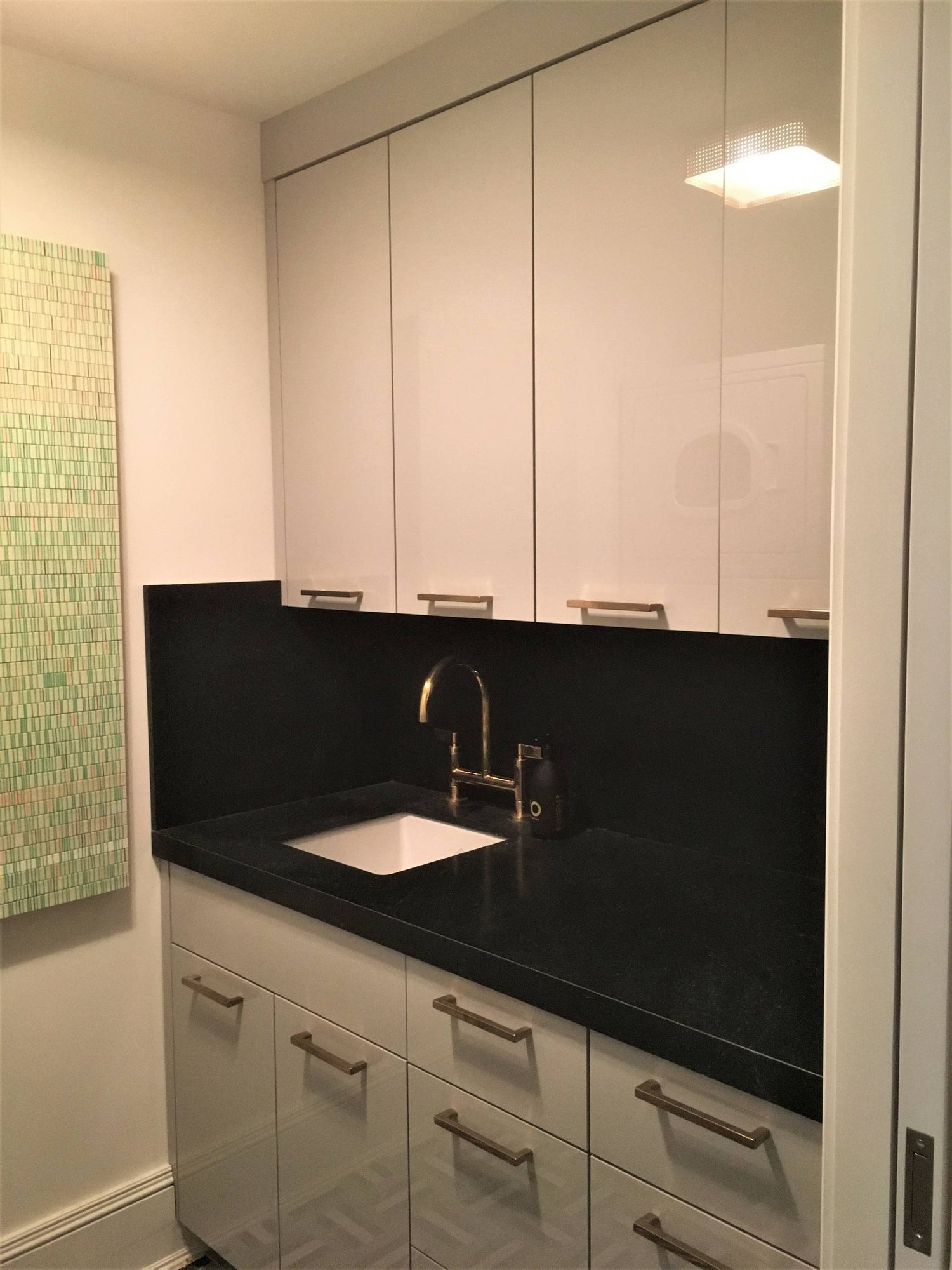 Mid-sized modern galley multicolored floor dedicated laundry room with an undermount sink, flat-panel cabinets, gray cabinets, white walls and a stacked washer/dryer, by Jensen Design in Telluride, CO