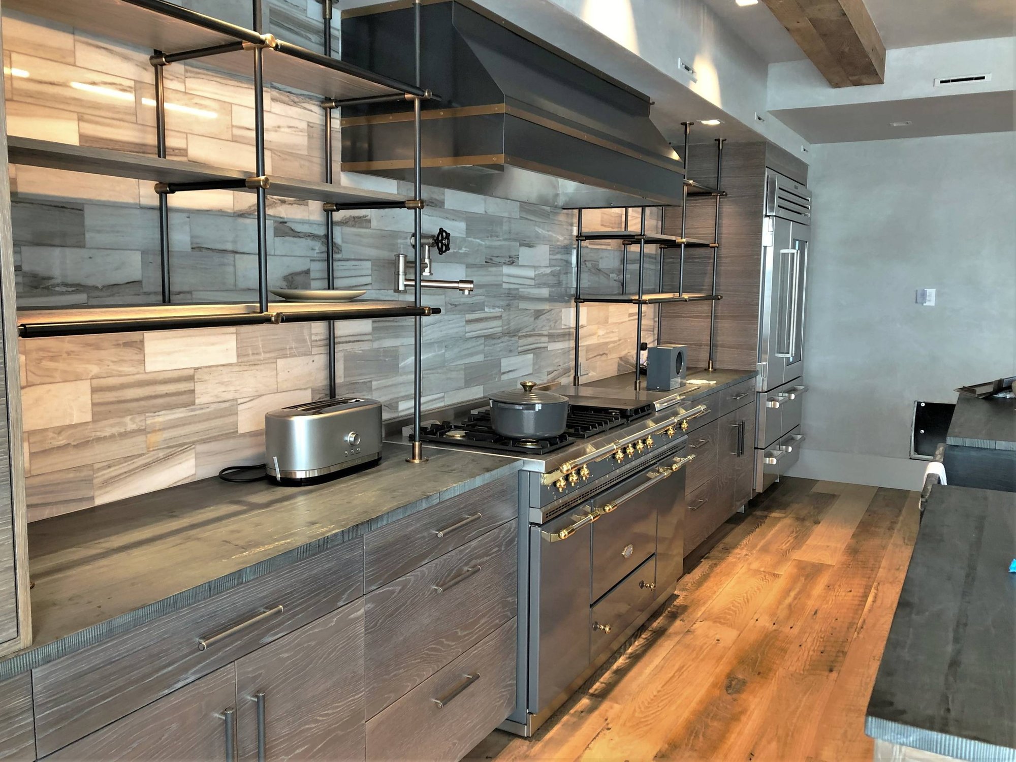 Large trendy u-shaped medium tone wood floor and brown floor eat-in kitchen with a farmhouse sink, flat-panel cabinets, light wood cabinets, quartzite countertops, beige backsplash, porcelain backsplash, stainless steel appliances, an island and black countertops, by Jensen Design in Mountain Villag