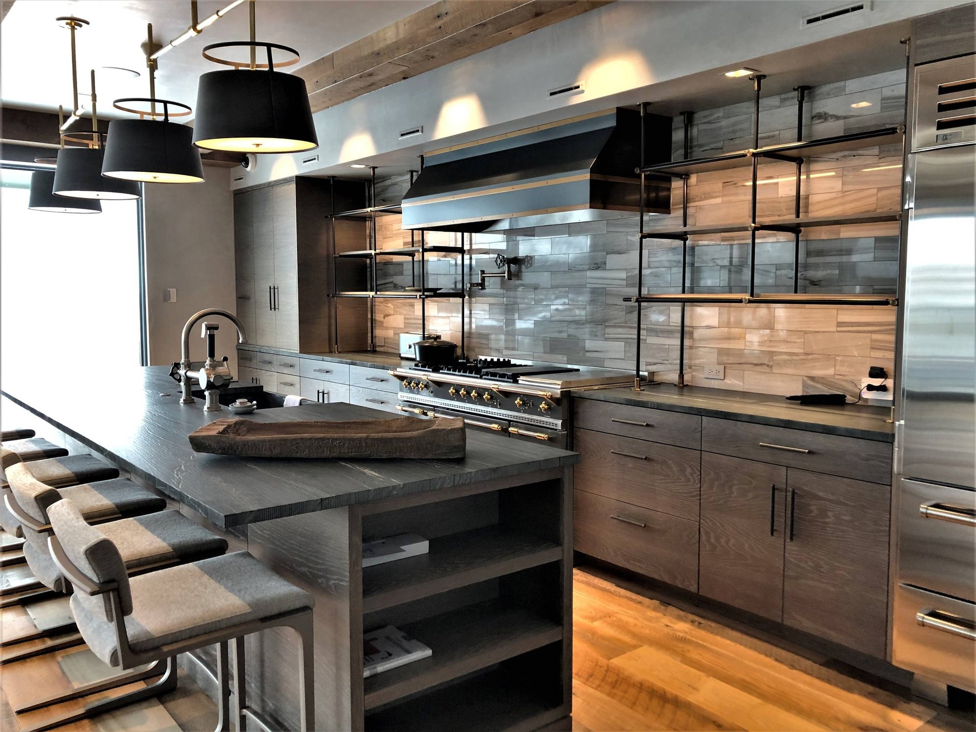 Large trendy u-shaped medium tone wood floor and brown floor eat-in kitchen with a farmhouse sink, flat-panel cabinets, light wood cabinets, quartzite countertops, beige backsplash, porcelain backsplash, stainless steel appliances, an island and black countertops, by Jensen Design in Mountain Villag