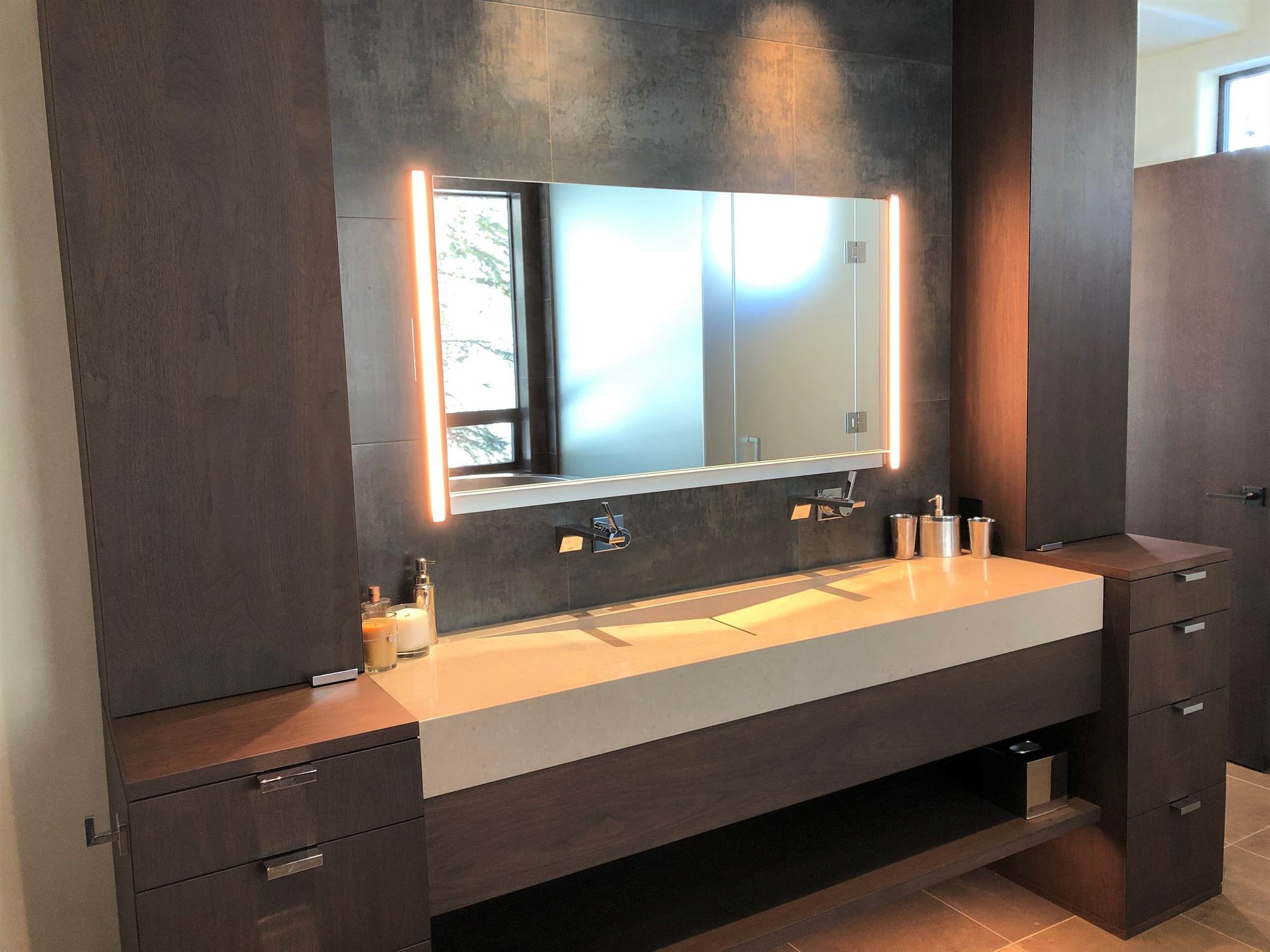 Mid-sized contemporary master gray tile brown floor and double-sink bathroom with flat-panel cabinets, dark wood cabinets, beige walls, a trough sink, a hinged shower door, beige countertops and a built-in vanity, by Jensen Design in Telluride, CO