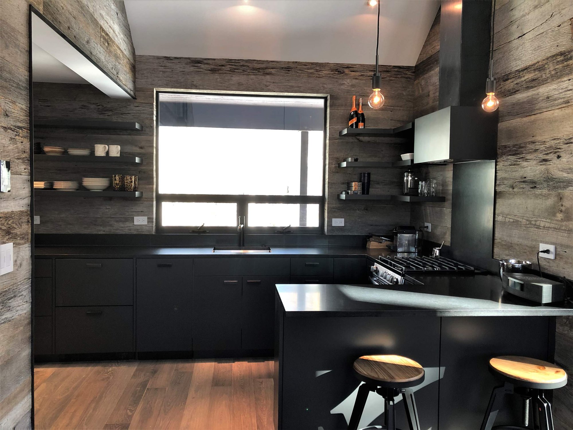 Mid-sized contemporary u-shaped light wood floor, orange floor and vaulted ceiling open concept kitchen with an undermount sink, flat-panel cabinets, black cabinets, brown backsplash, stainless steel appliances, a peninsula and brown countertops, by Jensen Design in Telluride, CO