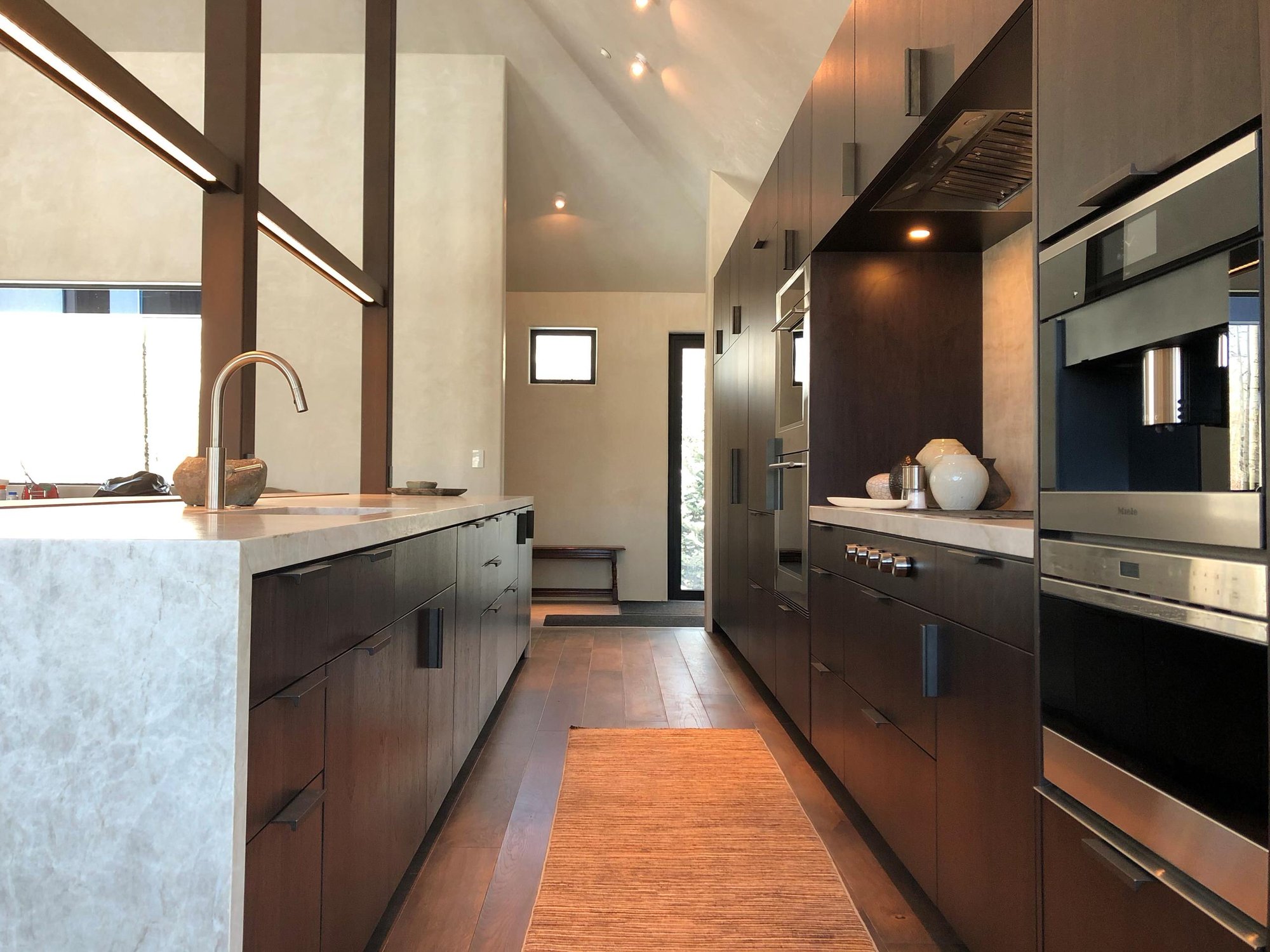 Large trendy galley medium tone wood floor, brown floor and vaulted ceiling open concept kitchen with an undermount sink, flat-panel cabinets, dark wood cabinets, colored appliances, an island and multicolored countertops, by Jensen Design in Telluride, CO