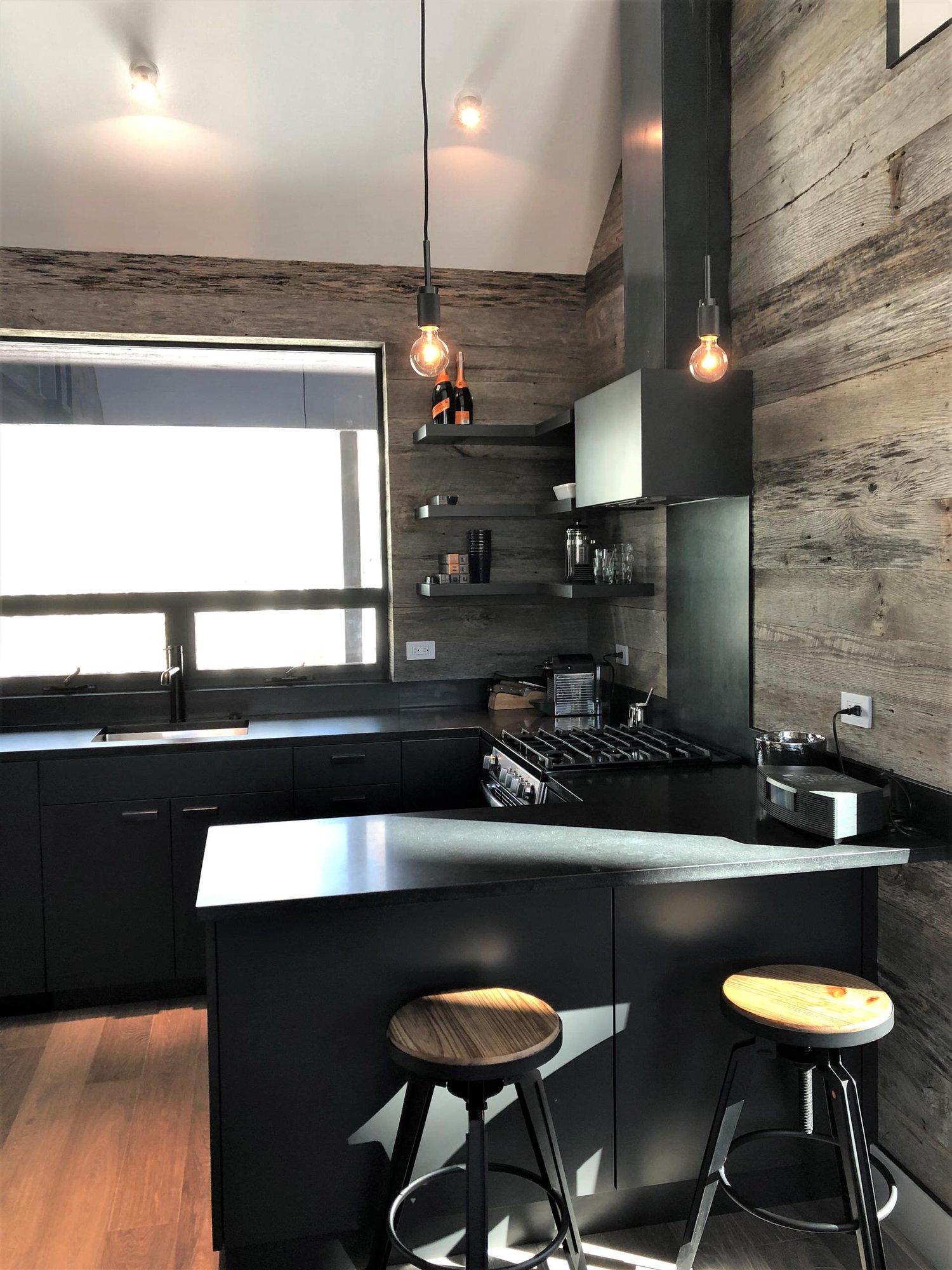 Mid-sized contemporary u-shaped light wood floor, orange floor and vaulted ceiling open concept kitchen with an undermount sink, flat-panel cabinets, black cabinets, brown backsplash, stainless steel appliances, a peninsula and brown countertops, by Jensen Design in Telluride, CO