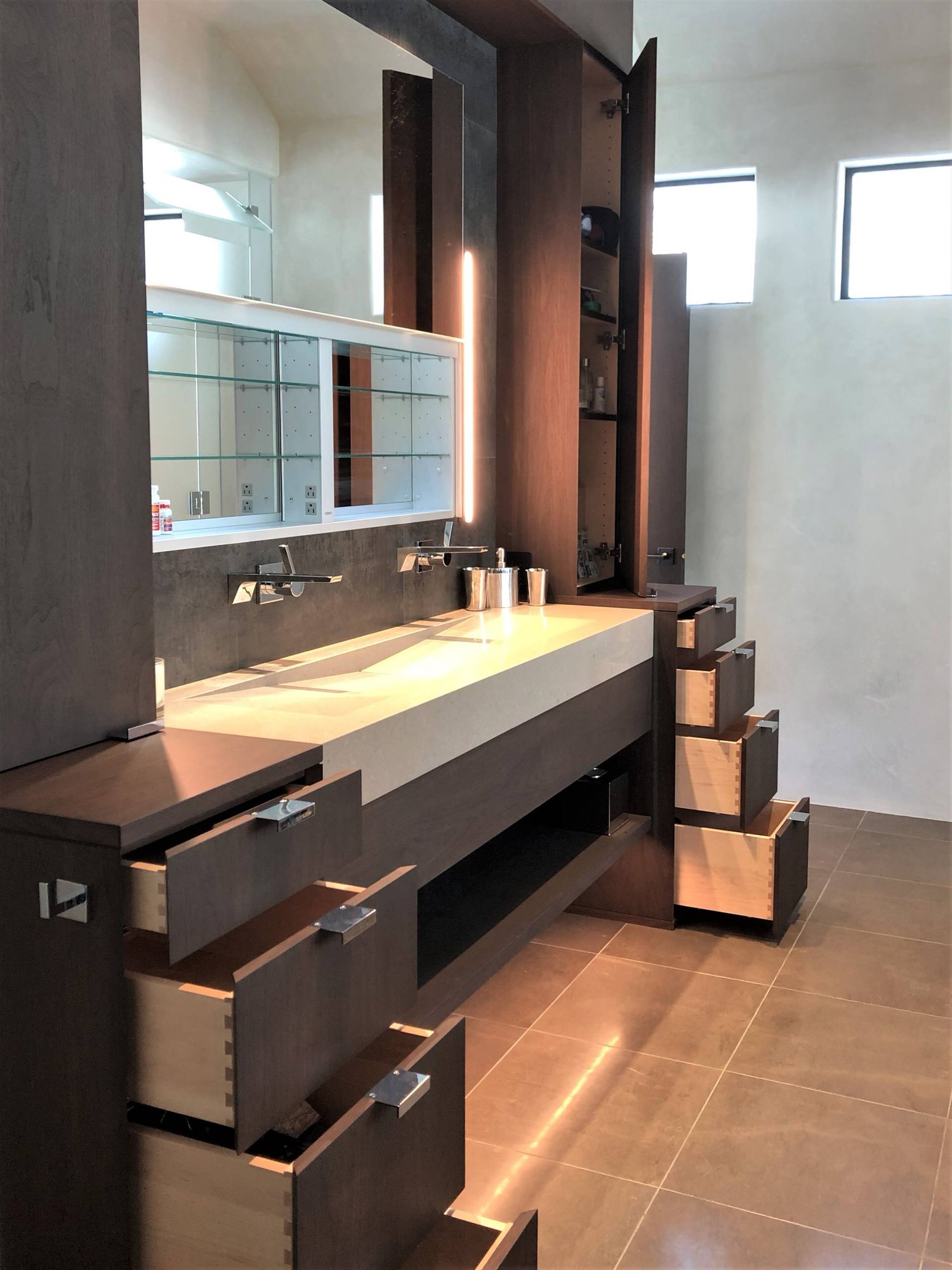Mid-sized trendy master gray tile brown floor and double-sink bathroom with flat-panel cabinets, dark wood cabinets, beige walls, a trough sink, a hinged shower door, beige countertops and a built-in vanity, by Jensen Design in Telluride, CO