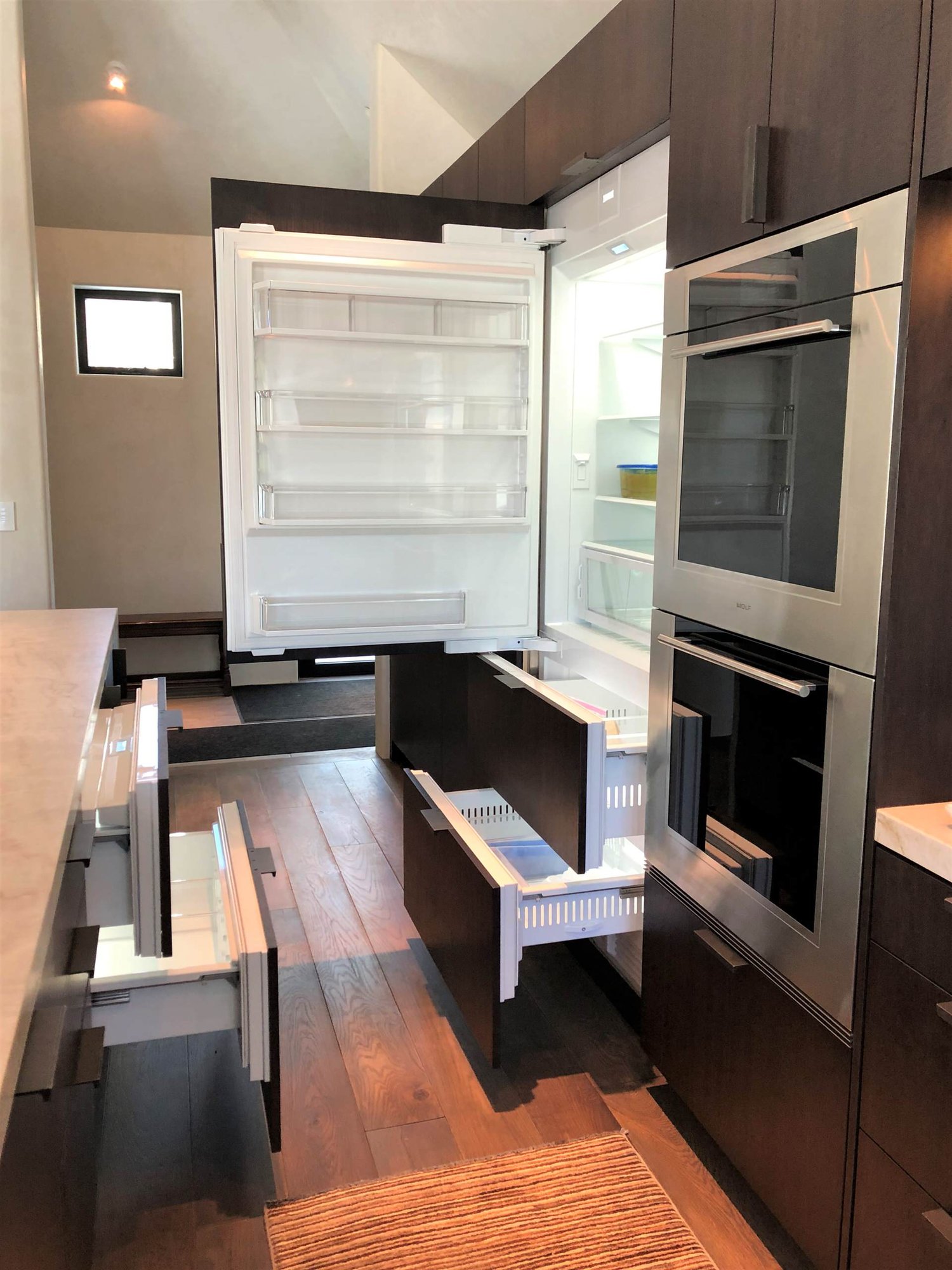 Large trendy galley medium tone wood floor, brown floor and vaulted ceiling open concept kitchen with an undermount sink, flat-panel cabinets, dark wood cabinets, colored appliances, an island and multicolored countertops, by Jensen Design in Telluride, CO