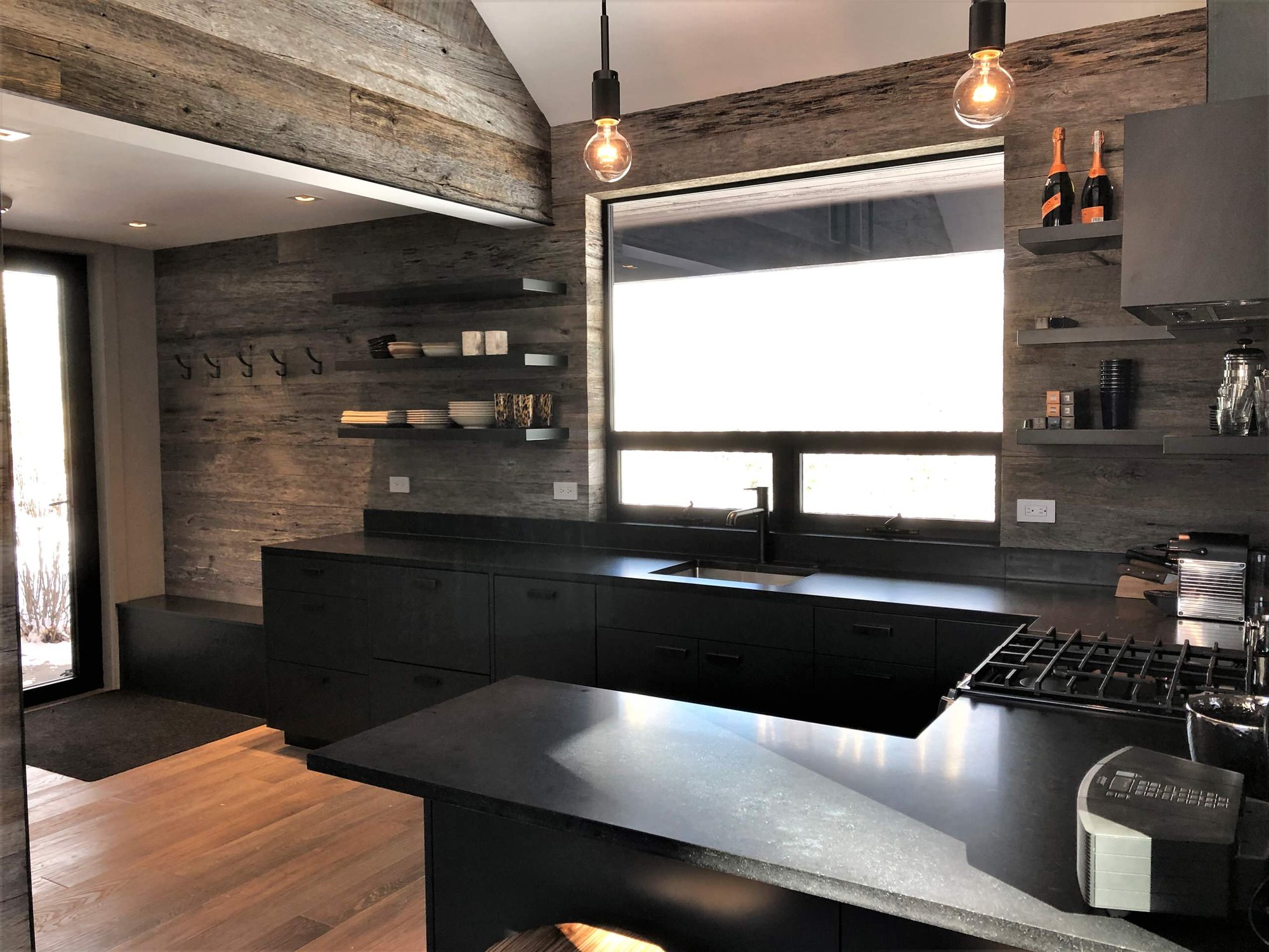 Mid-sized trendy u-shaped light wood floor, orange floor and vaulted ceiling open concept kitchen with an undermount sink, flat-panel cabinets, black cabinets, brown backsplash, stainless steel appliances, a peninsula and brown countertops, by Jensen Design in Telluride, CO