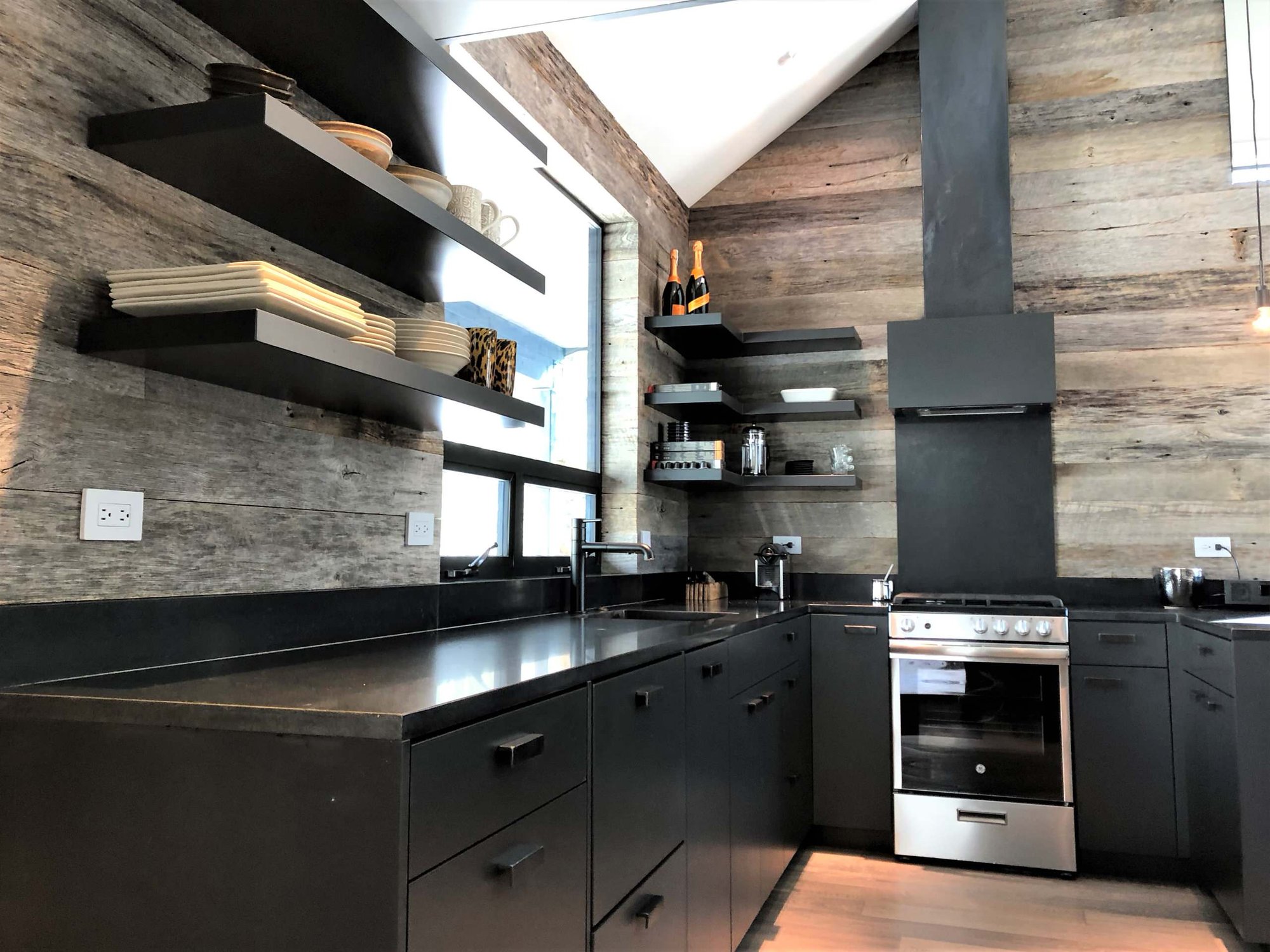 Mid-sized contemporary u-shaped light wood floor, orange floor and vaulted ceiling open concept kitchen with an undermount sink, flat-panel cabinets, black cabinets, brown backsplash, stainless steel appliances, a peninsula and brown countertops, by Jensen Design in Telluride, CO