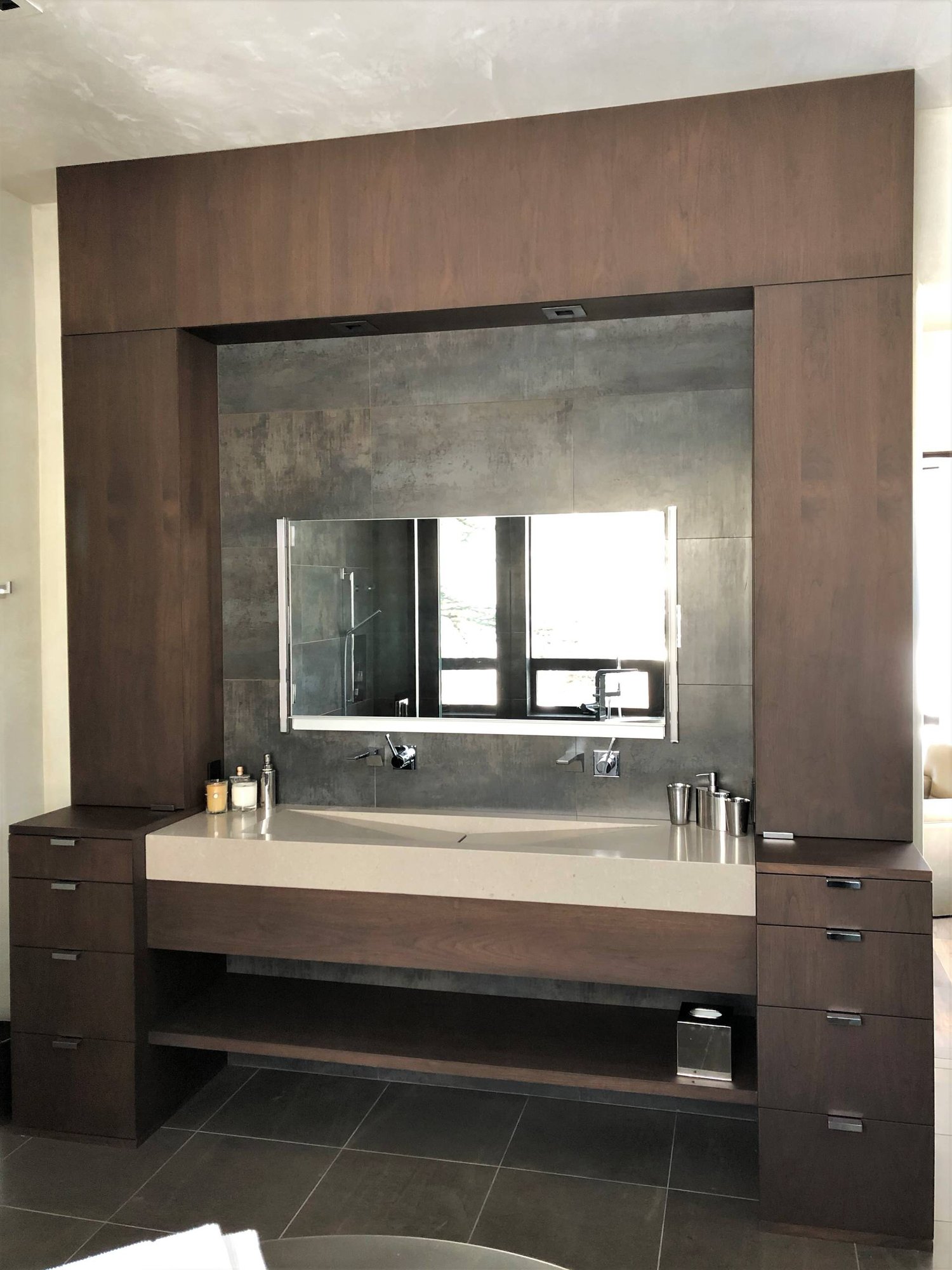 Mid-sized trendy master gray tile brown floor and double-sink bathroom with flat-panel cabinets, dark wood cabinets, beige walls, a trough sink, a hinged shower door, beige countertops and a built-in vanity, by Jensen Design in Telluride, CO