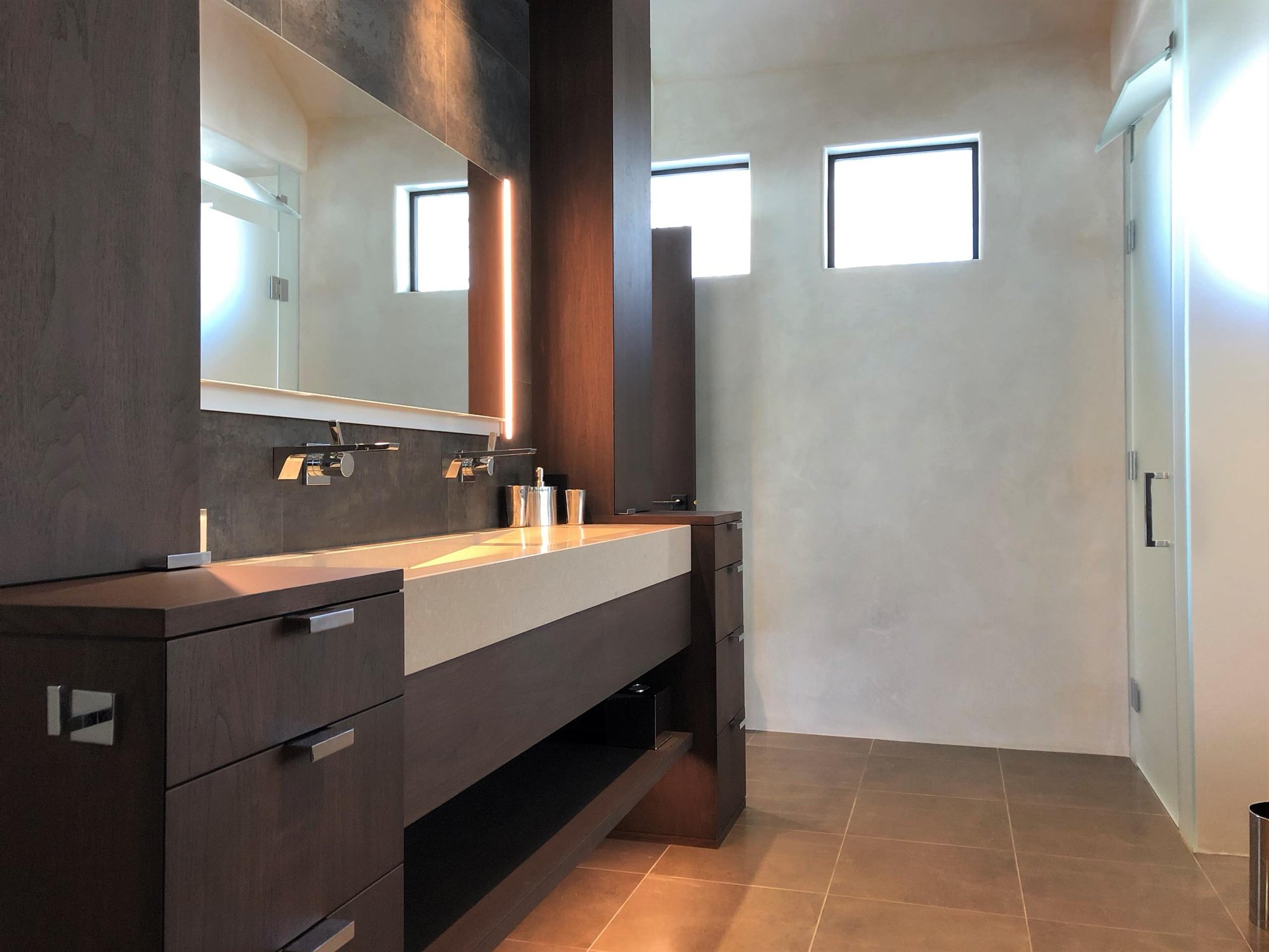 Mid-sized contemporary master gray tile brown floor and double-sink bathroom with flat-panel cabinets, dark wood cabinets, beige walls, a trough sink, a hinged shower door, beige countertops and a built-in vanity, by Jensen Design in Telluride, CO