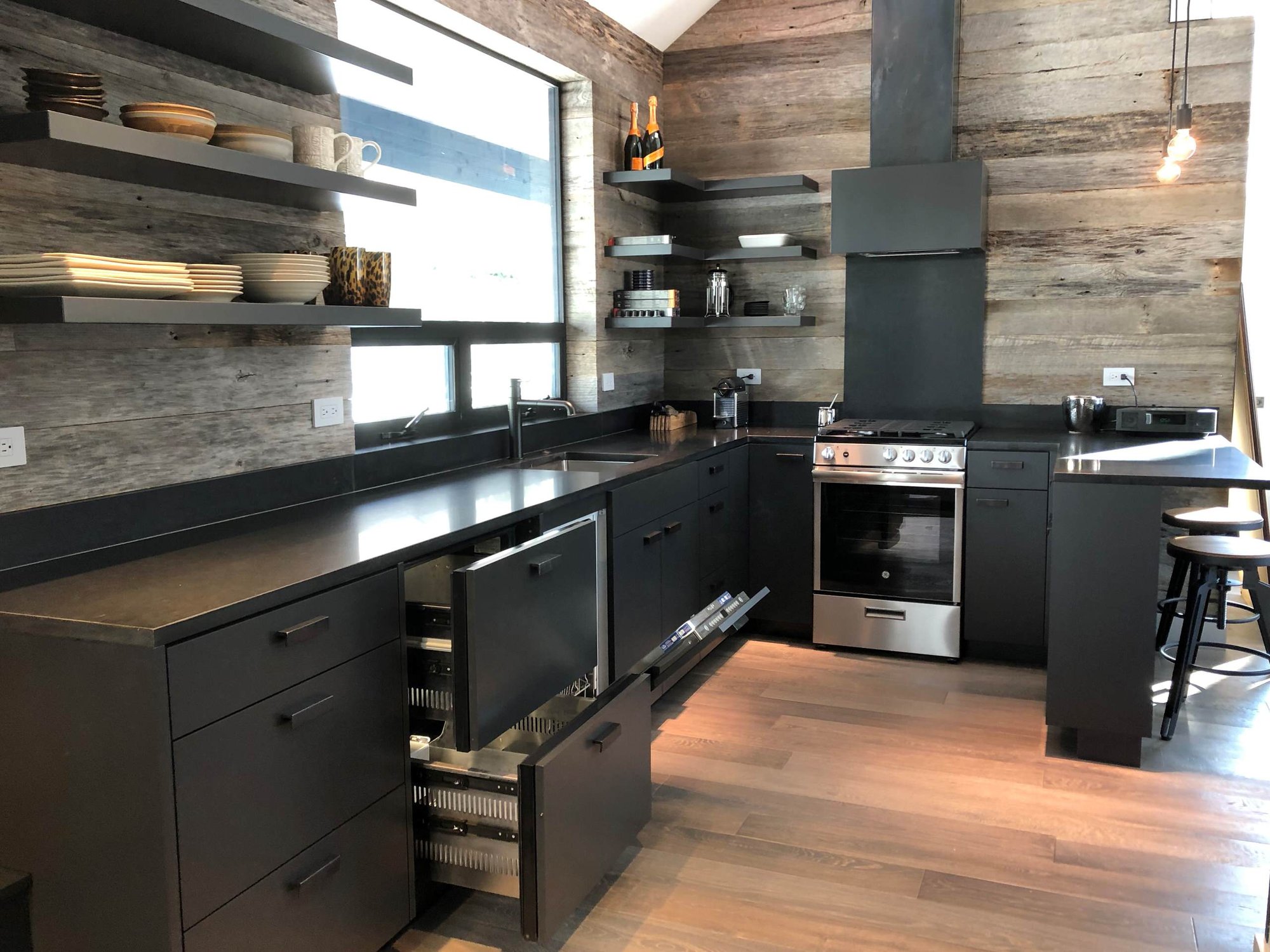 Mid-sized trendy u-shaped light wood floor, orange floor and vaulted ceiling open concept kitchen with an undermount sink, flat-panel cabinets, black cabinets, brown backsplash, stainless steel appliances, a peninsula and brown countertops, by Jensen Design in Telluride, CO