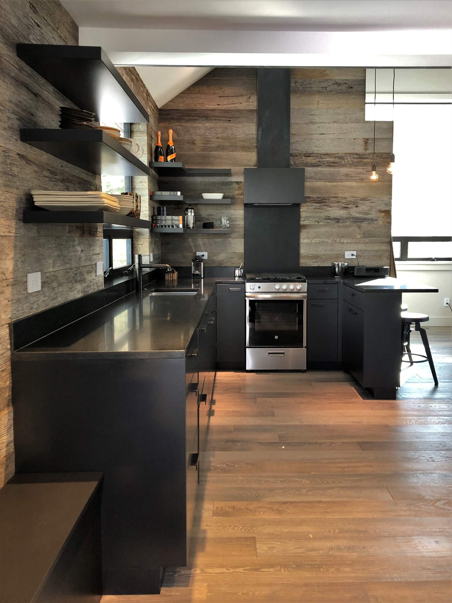 Mid-sized contemporary u-shaped light wood floor, orange floor and vaulted ceiling open concept kitchen with an undermount sink, flat-panel cabinets, black cabinets, brown backsplash, stainless steel appliances, a peninsula and brown countertops, by Jensen Design in Telluride, CO