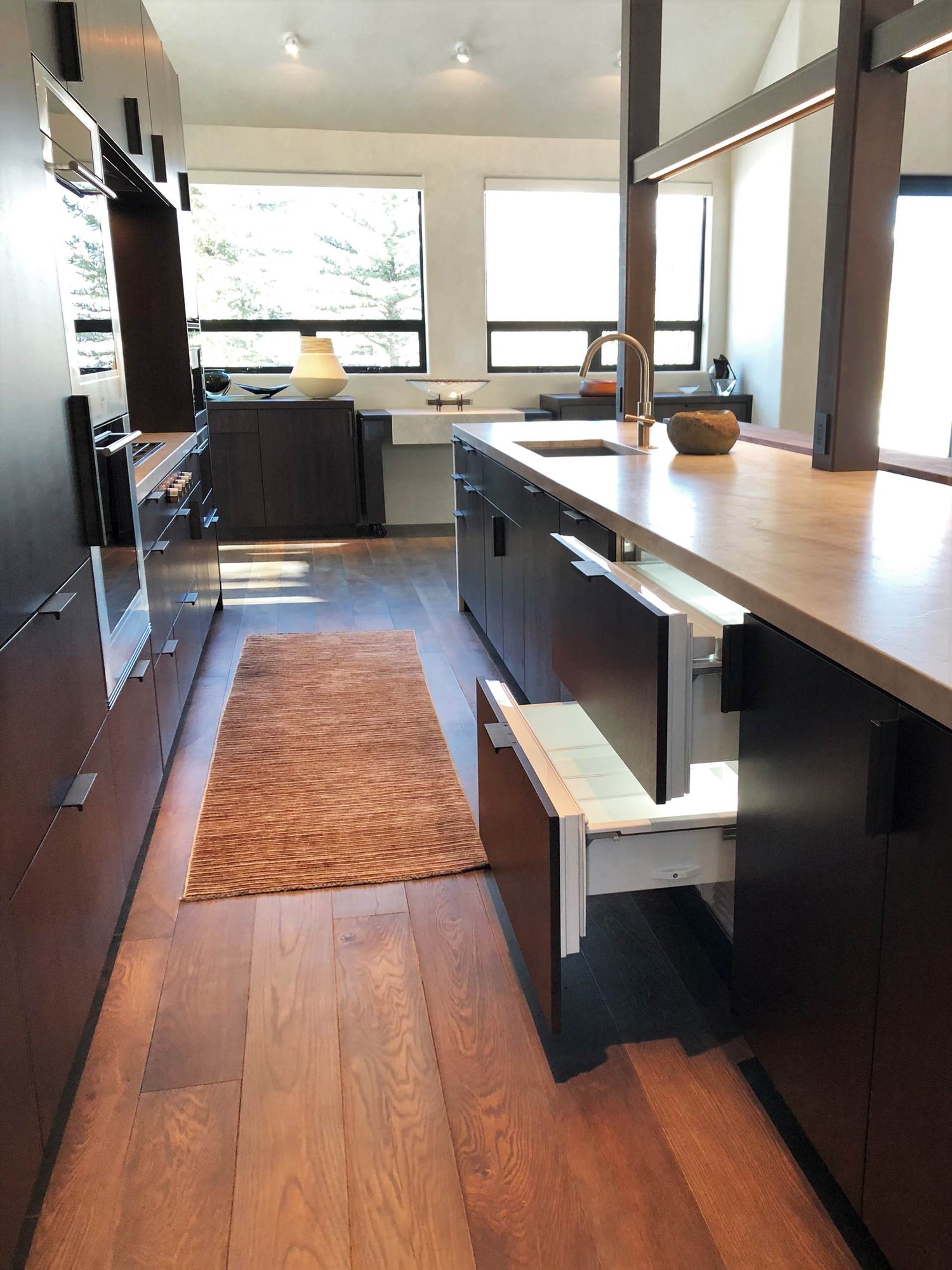 Large trendy galley medium tone wood floor, brown floor and vaulted ceiling open concept kitchen with an undermount sink, flat-panel cabinets, dark wood cabinets, colored appliances, an island and multicolored countertops, by Jensen Design in Telluride, CO