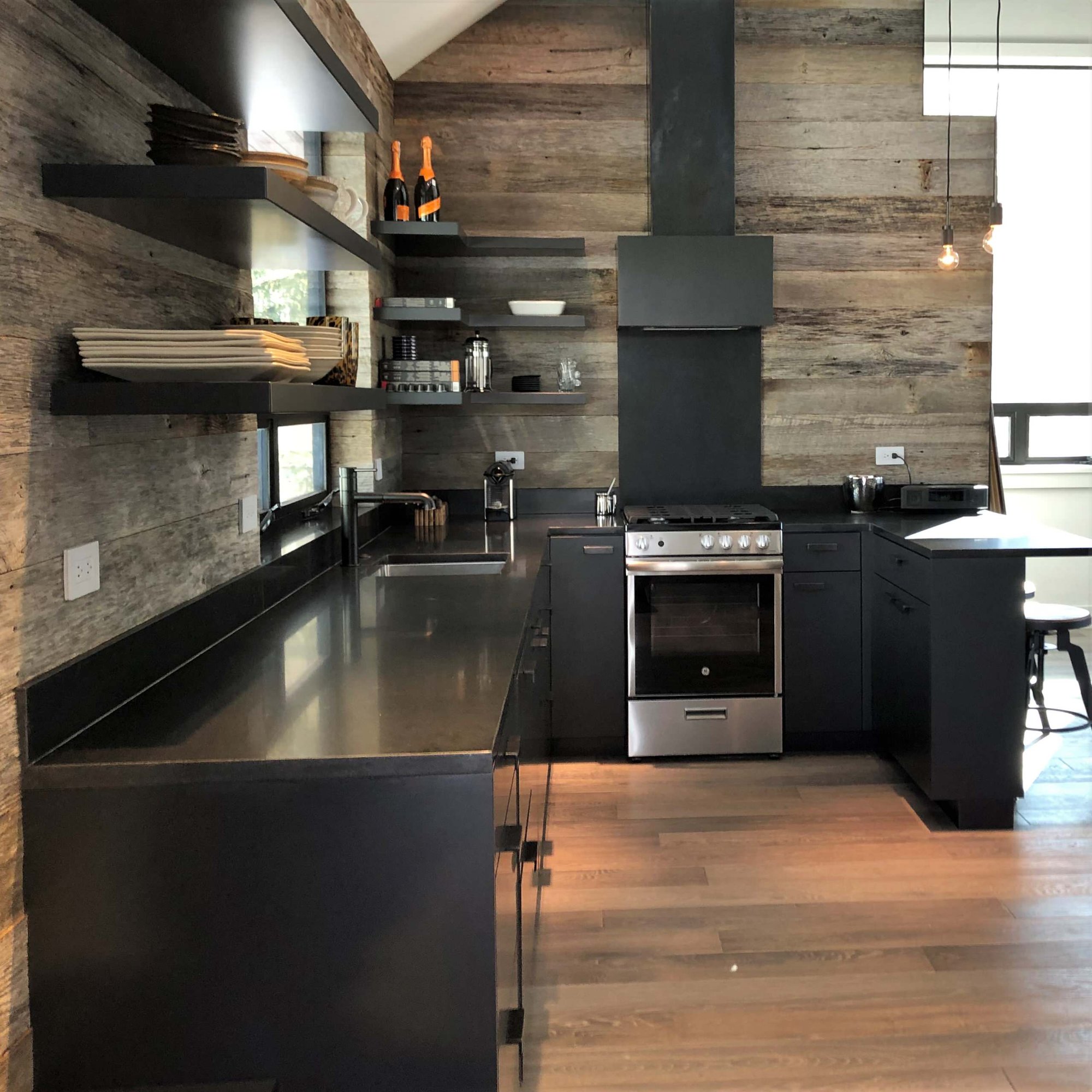 Mid-sized contemporary u-shaped light wood floor, orange floor and vaulted ceiling open concept kitchen with an undermount sink, flat-panel cabinets, black cabinets, brown backsplash, stainless steel appliances, a peninsula and brown countertops, by Jensen Design in Telluride, CO
