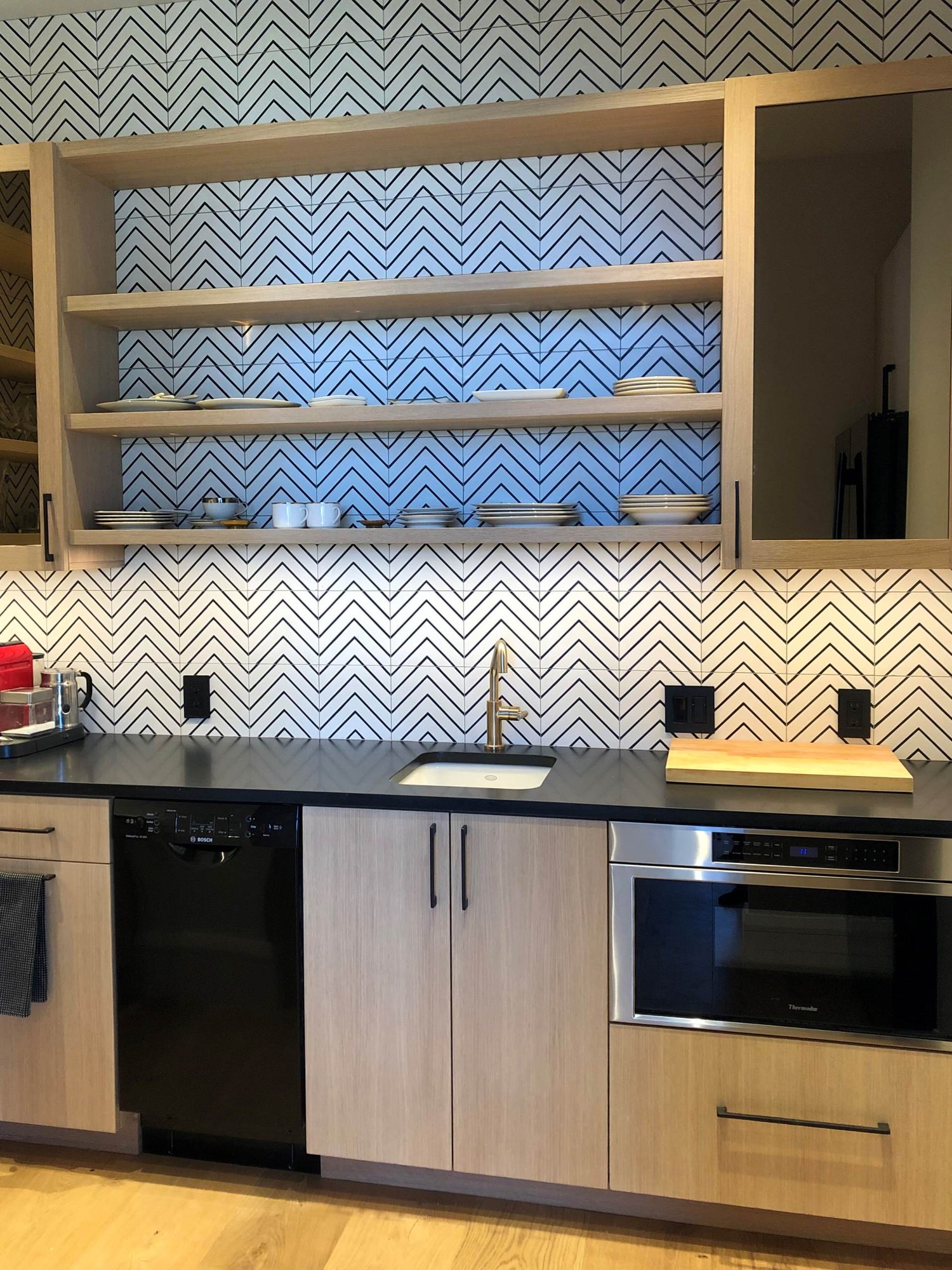 Mid-sized trendy u-shaped medium tone wood floor and brown floor kitchen pantry with an undermount sink, flat-panel cabinets, light wood cabinets, white backsplash, black appliances and black countertops, by Jensen Design in Telluride, CO