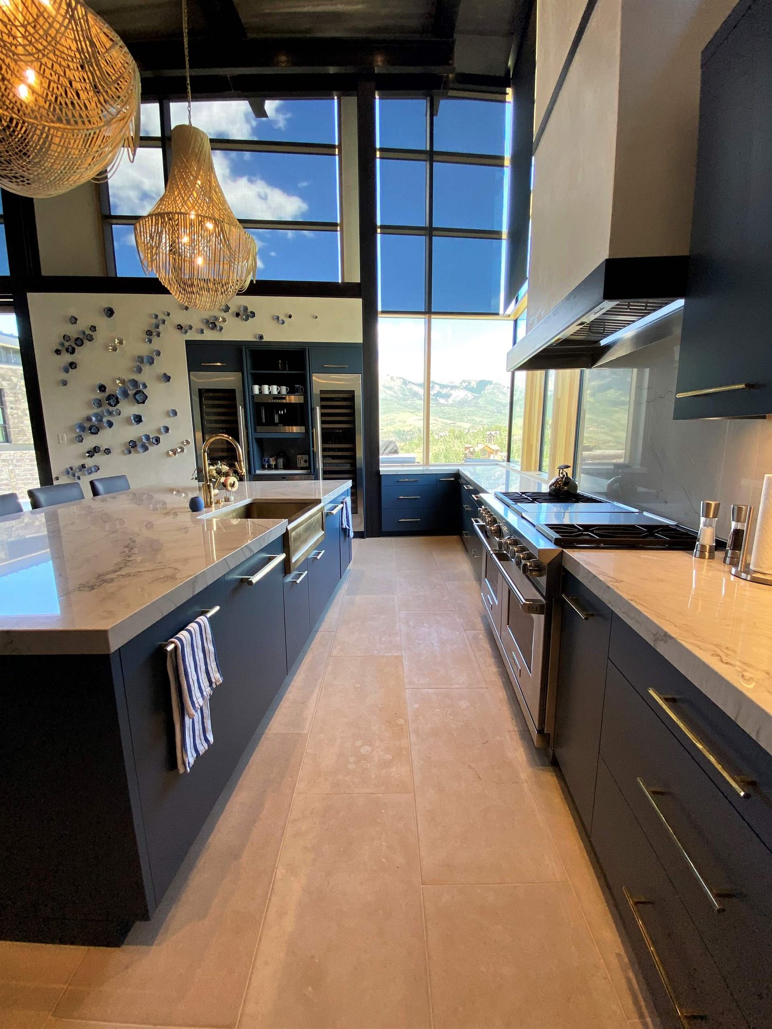 Large contemporary u-shaped limestone floor, gray floor and wood ceiling open concept kitchen with a farmhouse sink, flat-panel cabinets, blue cabinets, marble countertops, white backsplash, marble backsplash, paneled appliances, an island and white countertops, by Jensen Design in Telluride, CO