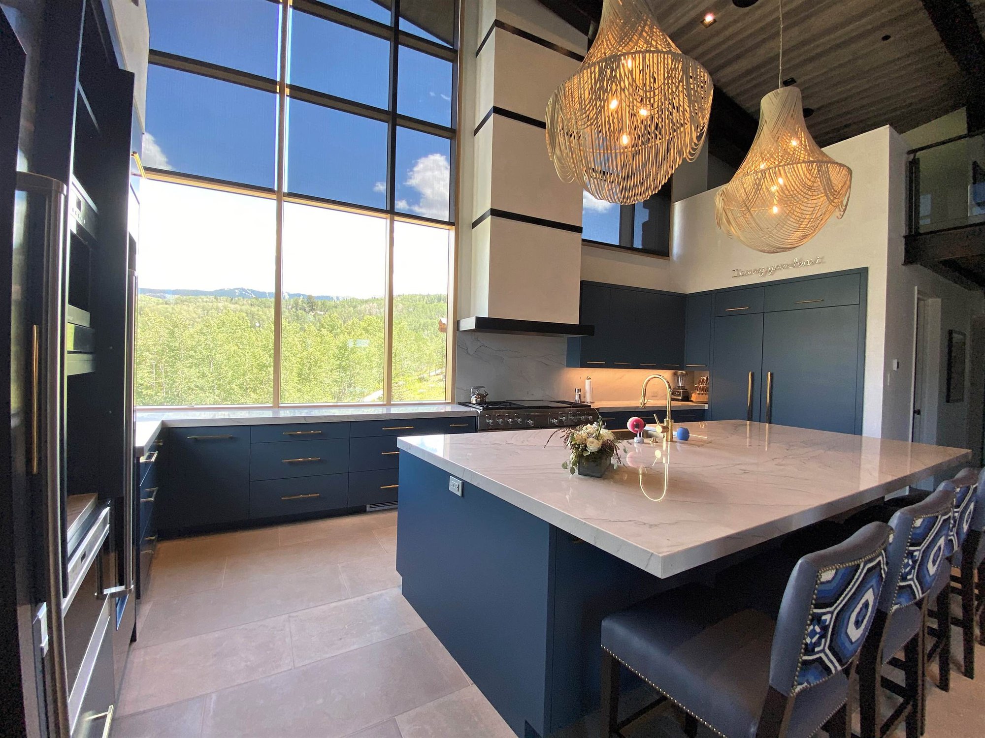 Large contemporary u-shaped limestone floor, gray floor and wood ceiling open concept kitchen with a farmhouse sink, flat-panel cabinets, blue cabinets, marble countertops, white backsplash, marble backsplash, paneled appliances, an island and white countertops, by Jensen Design in Telluride, CO