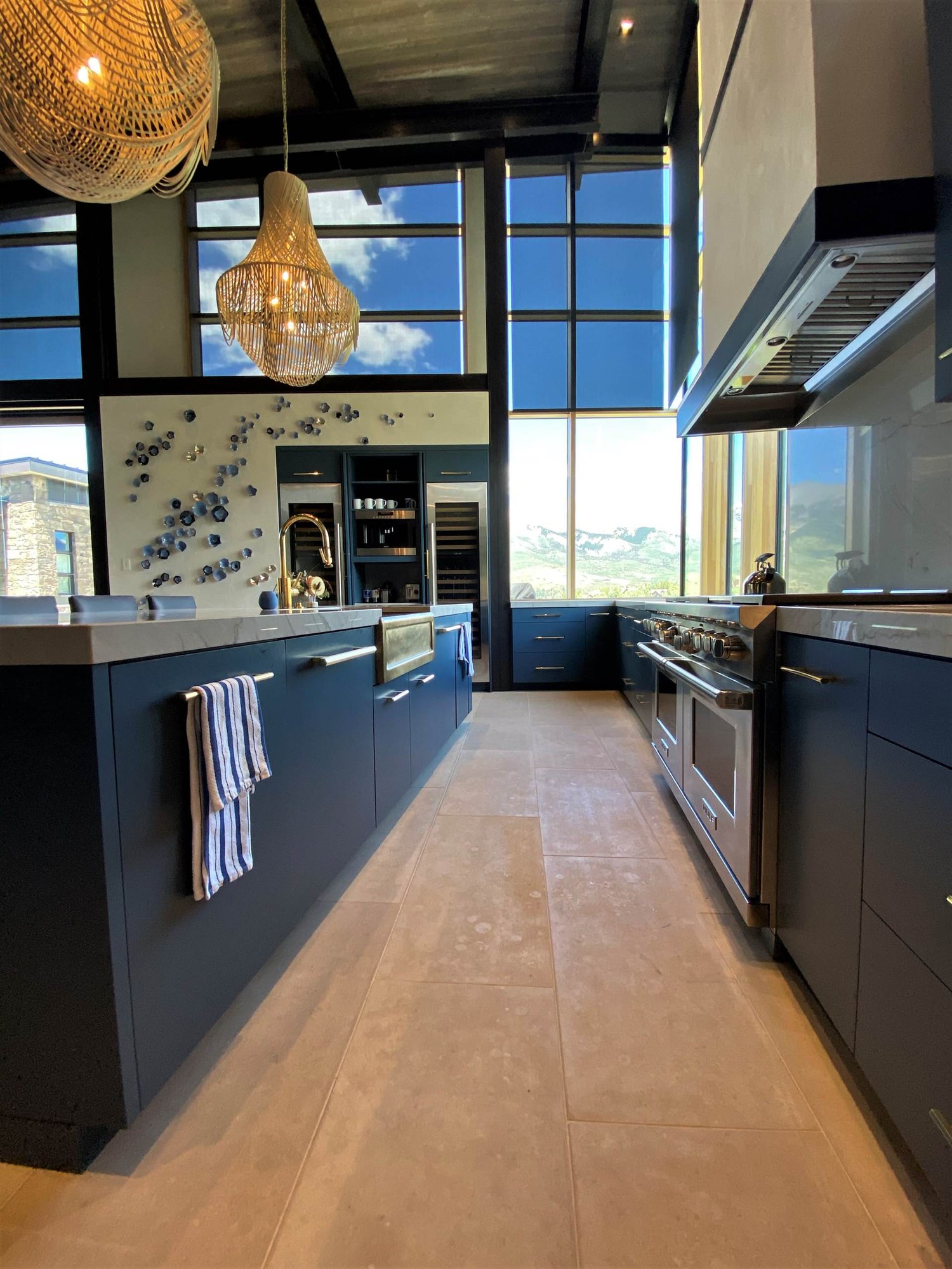 Large contemporary u-shaped limestone floor, gray floor and wood ceiling open concept kitchen with a farmhouse sink, flat-panel cabinets, blue cabinets, marble countertops, white backsplash, marble backsplash, paneled appliances, an island and white countertops, by Jensen Design in Telluride, CO