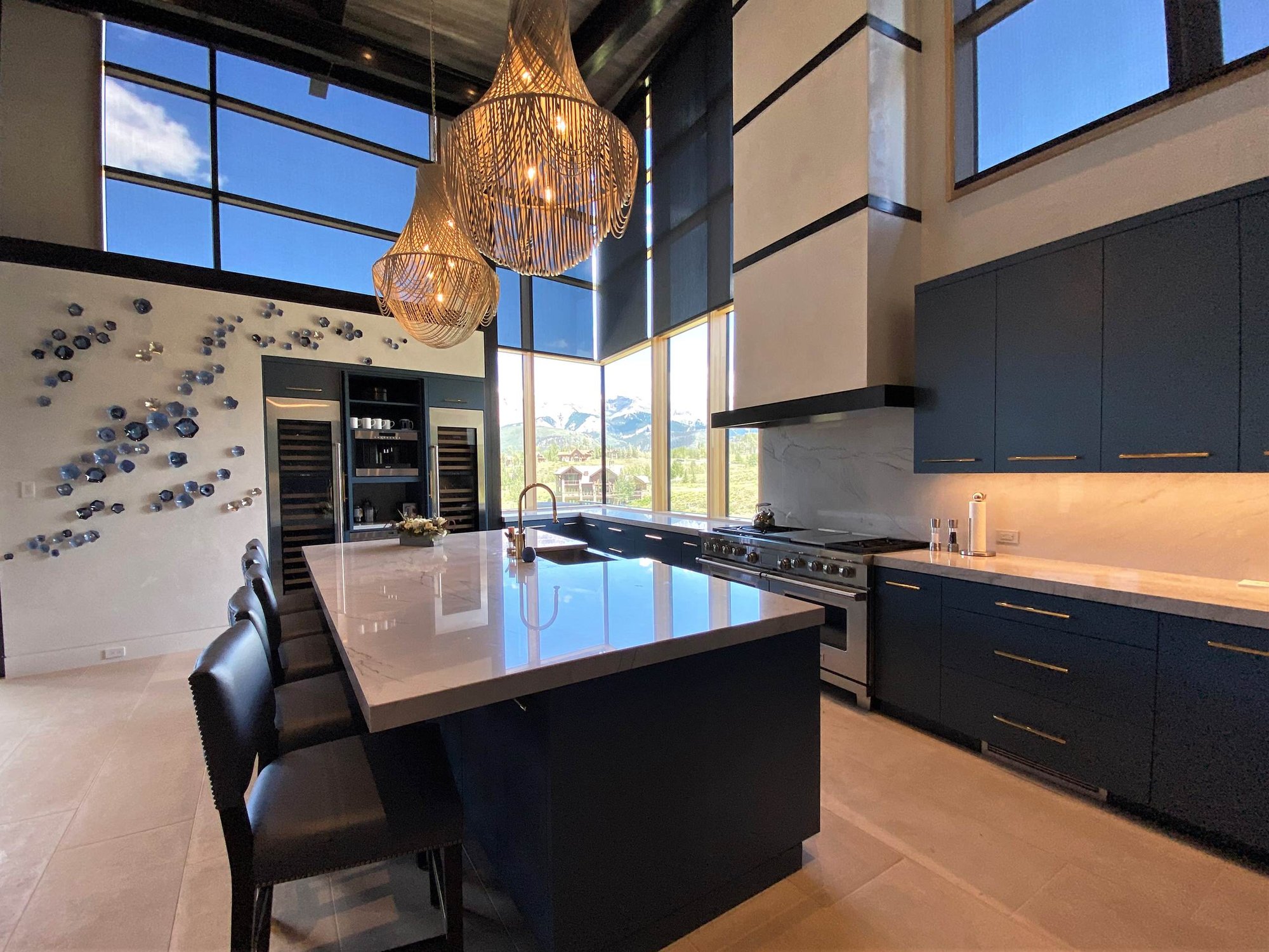 Large trendy u-shaped limestone floor, gray floor and wood ceiling open concept kitchen with a farmhouse sink, flat-panel cabinets, blue cabinets, marble countertops, white backsplash, marble backsplash, paneled appliances, an island and white countertops, by Jensen Design in Telluride, CO