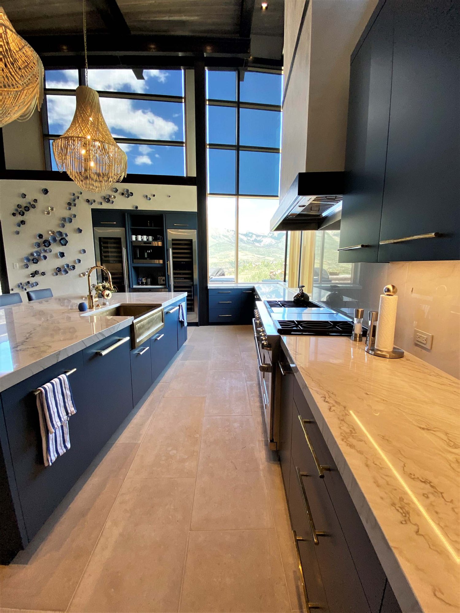 Large contemporary u-shaped limestone floor, gray floor and wood ceiling open concept kitchen with a farmhouse sink, flat-panel cabinets, blue cabinets, marble countertops, white backsplash, marble backsplash, paneled appliances, an island and white countertops, by Jensen Design in Telluride, CO