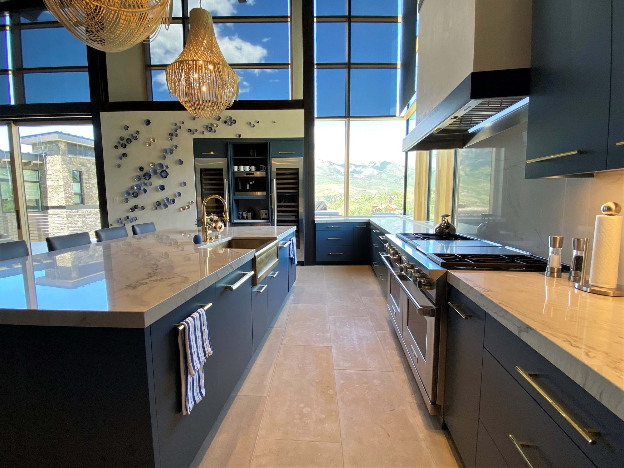 Large contemporary u-shaped limestone floor, gray floor and wood ceiling open concept kitchen with a farmhouse sink, flat-panel cabinets, blue cabinets, marble countertops, white backsplash, marble backsplash, paneled appliances, an island and white countertops, by Jensen Design in Telluride, CO