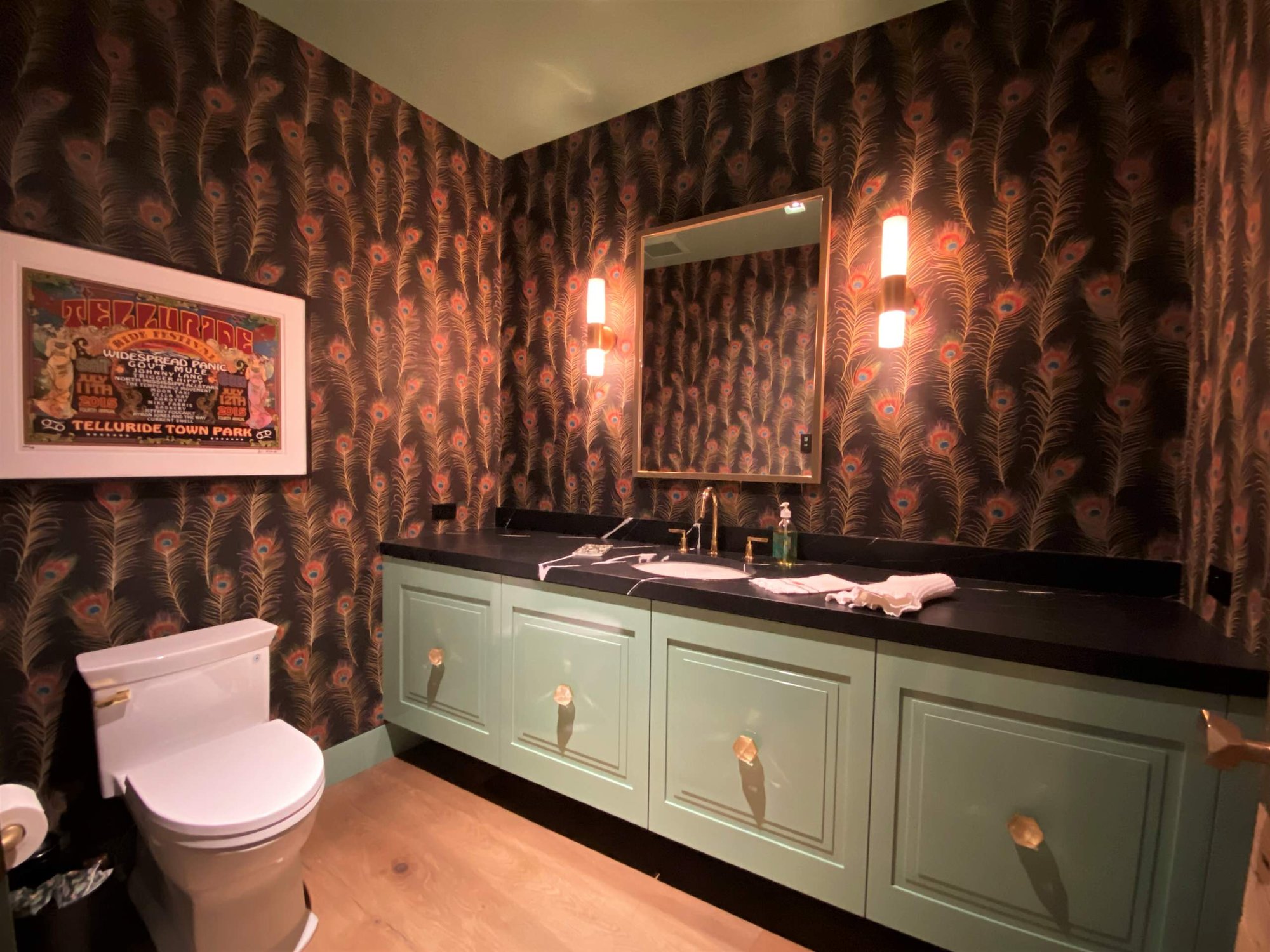 Mid-sized eclectic 3/4 light wood floor, brown floor, single-sink and wallpaper bathroom with raised-panel cabinets, green cabinets, a two-piece toilet, an undermount sink, black countertops and a floating vanity, by Jensen Design in Telluride, CO