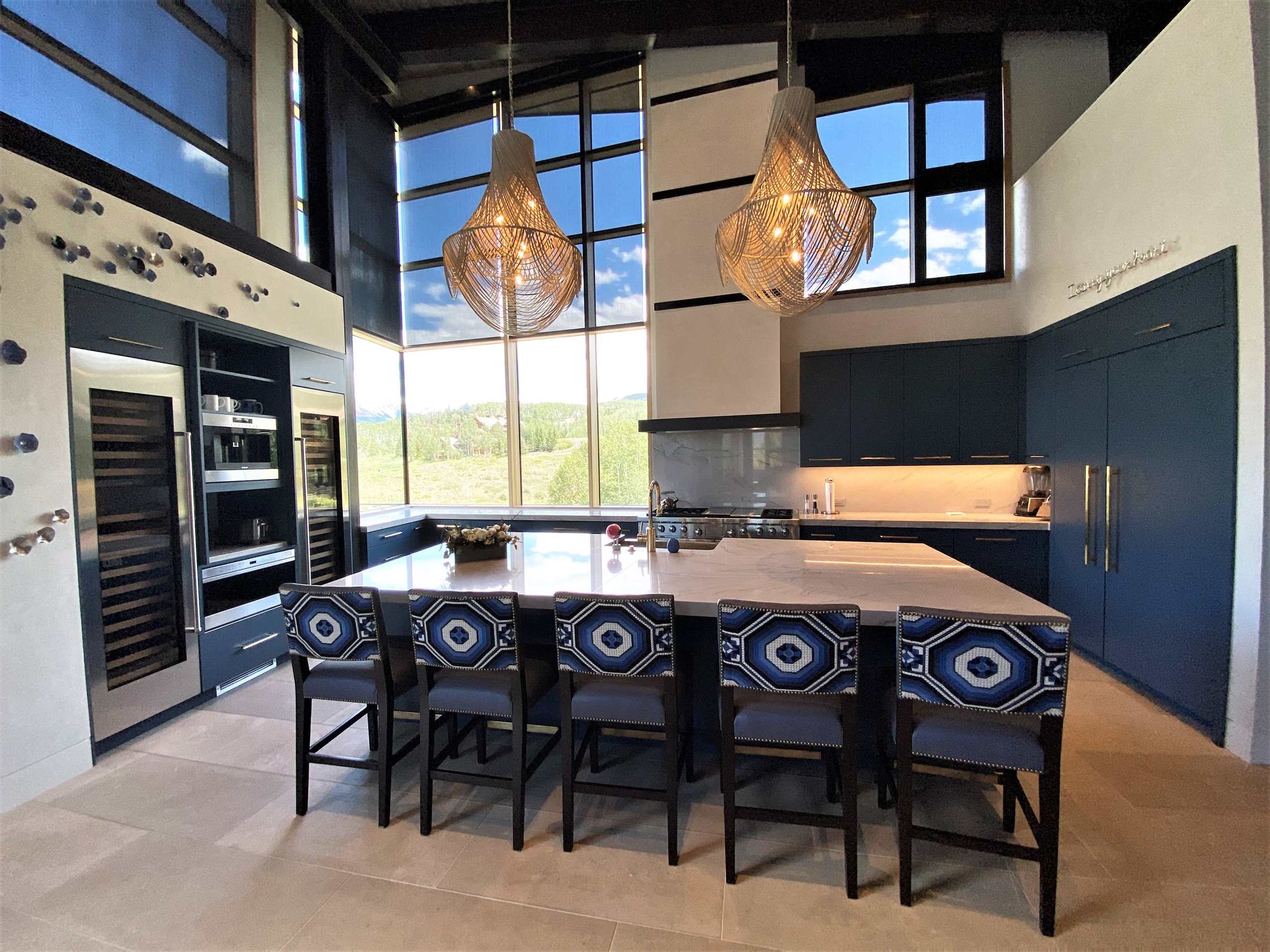 Large trendy u-shaped limestone floor, gray floor and wood ceiling open concept kitchen with a farmhouse sink, flat-panel cabinets, blue cabinets, marble countertops, white backsplash, marble backsplash, paneled appliances, an island and white countertops, by Jensen Design in Telluride, CO