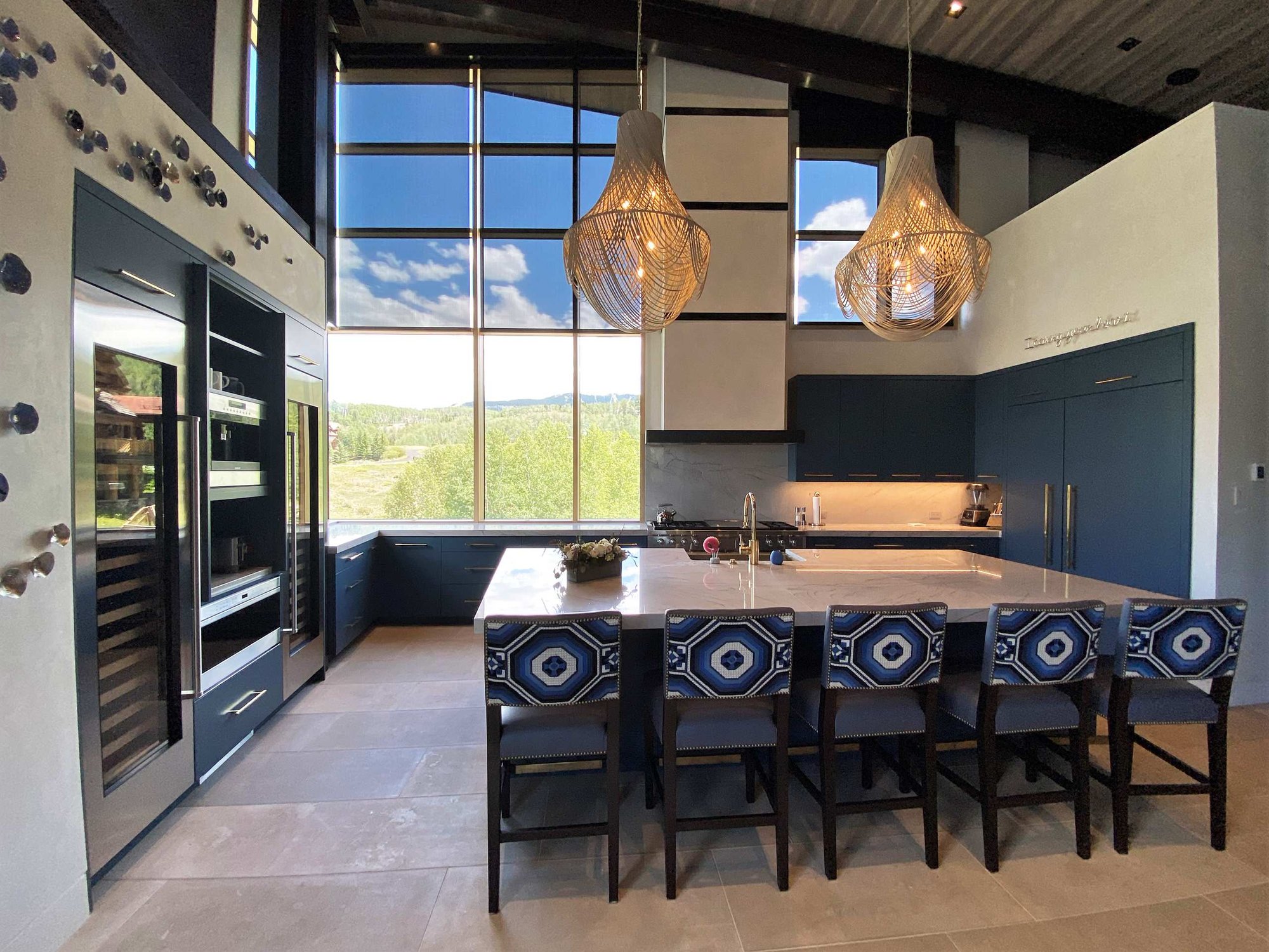 Large contemporary u-shaped limestone floor, gray floor and wood ceiling open concept kitchen with a farmhouse sink, flat-panel cabinets, blue cabinets, marble countertops, white backsplash, marble backsplash, paneled appliances, an island and white countertops, by Jensen Design in Telluride, CO